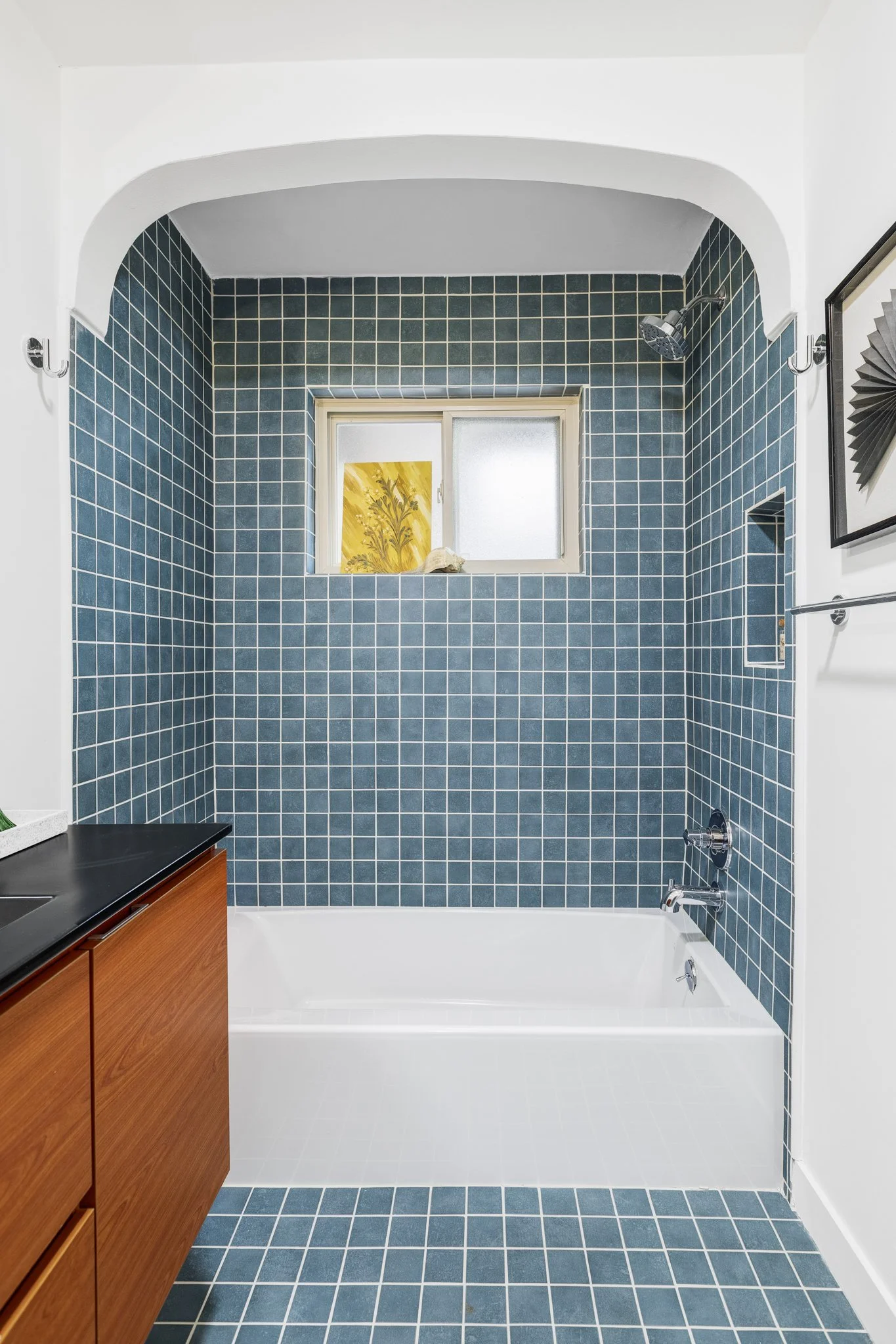 Bathroom with blue tiled shower area, small window, and a wooden vanity cabinet.