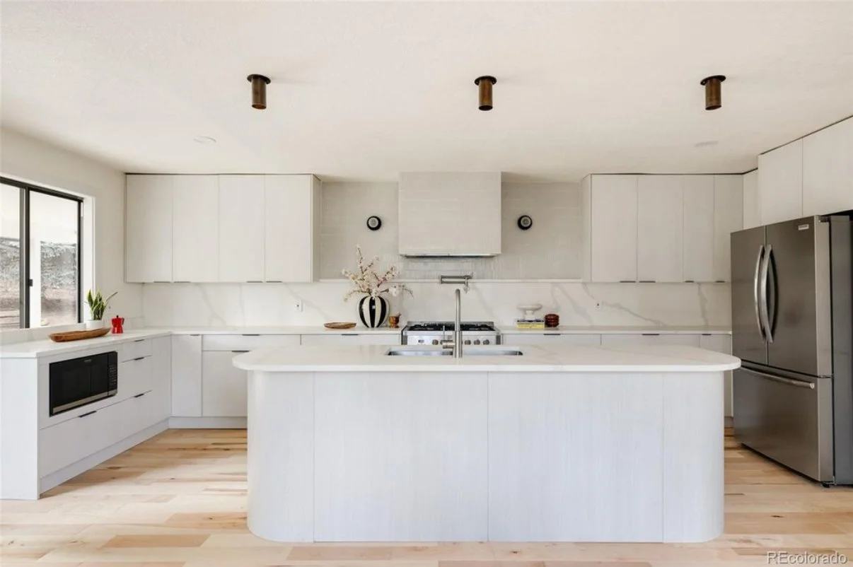 Modern kitchen with white cabinetry, marble backsplash, stainless steel refrigerator, and a central island with a sink.