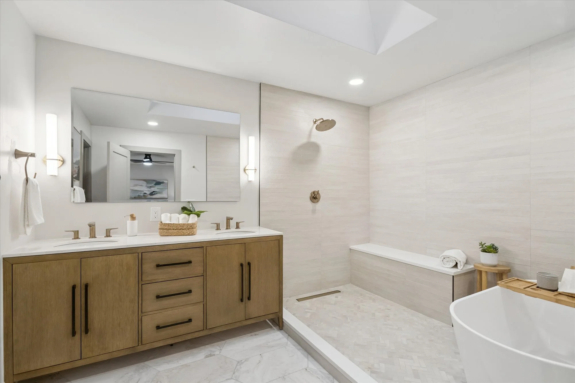 Modern bathroom with a wooden vanity, large mirror, walk-in shower with a rainfall showerhead, white bathtub, and minimalist decor including towels and a potted plant.