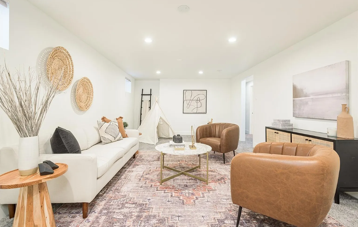 Living room with white sofa, brown leather chairs, a round marble coffee table, a black and wooden sideboard, and decorative wall art and baskets.