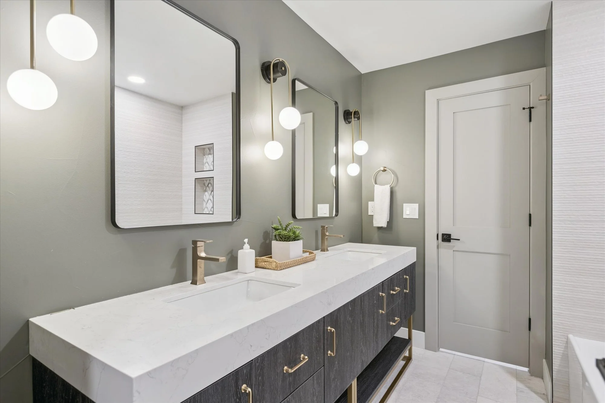 Modern bathroom with a double sink vanity, two mirrors, and wall-mounted light fixtures, gray walls, and a closed door.