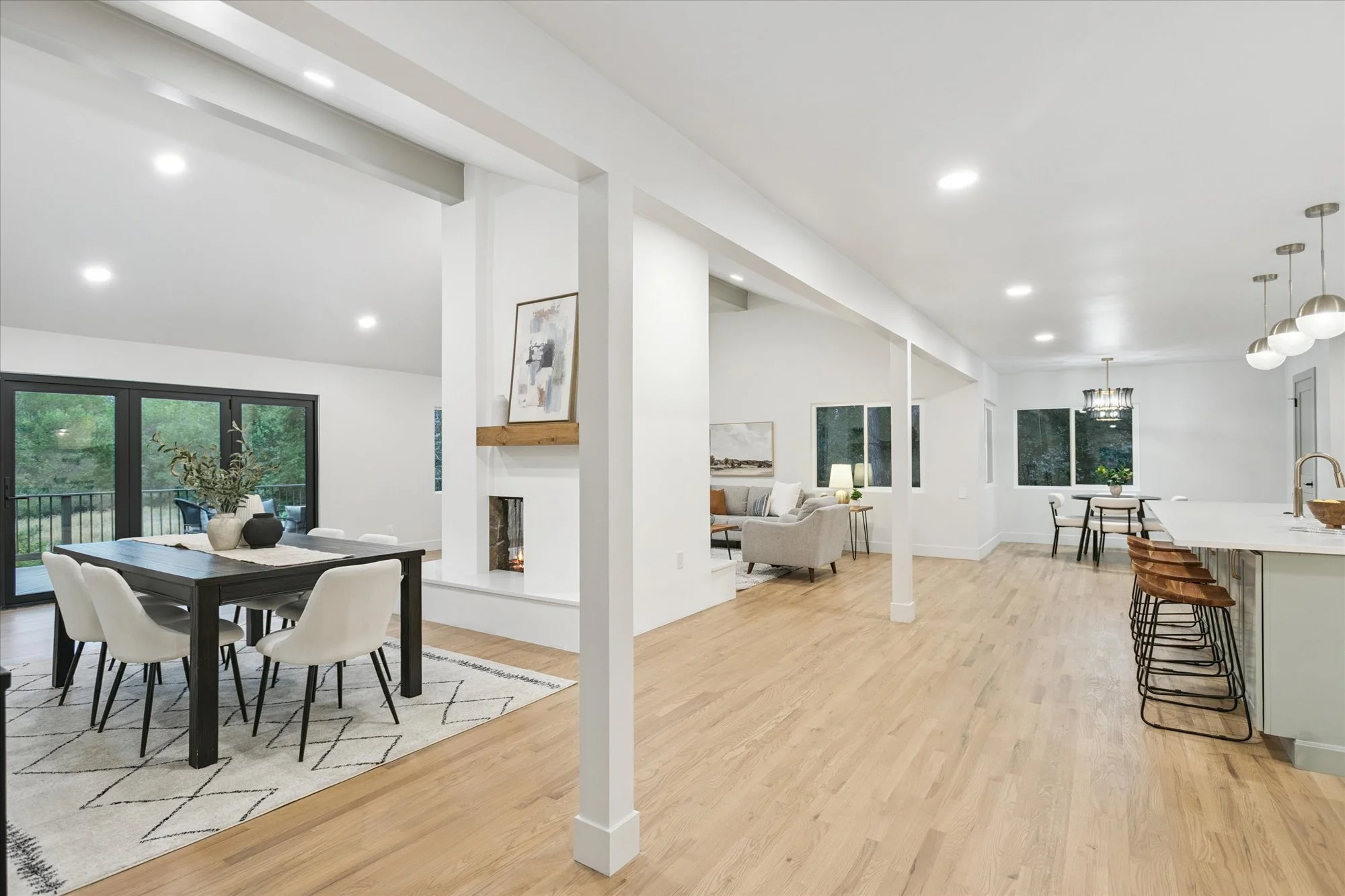 Open-concept living and dining area with hardwood floors, white walls, modern furniture, and large windows.