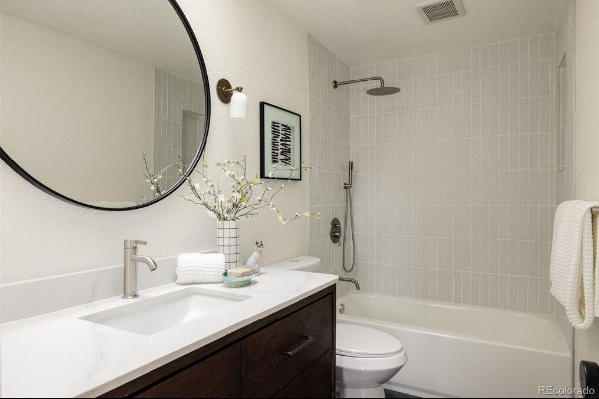 Modern bathroom with a white vanity, round mirror, and walk-in shower with tiled walls.