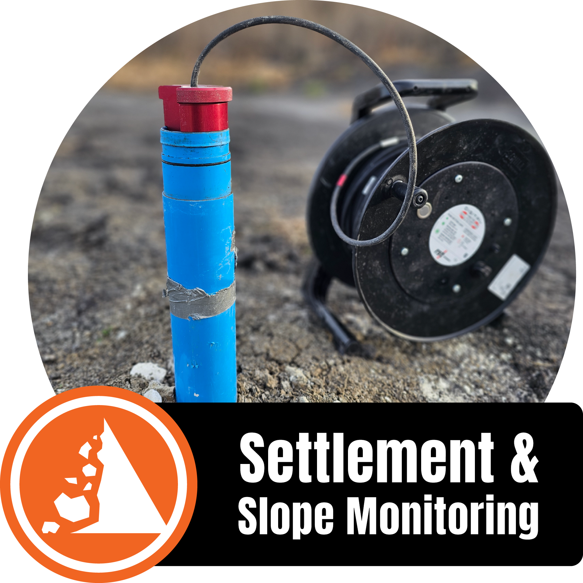 A blue marker post with red and blue bands next to a black retractable hose reel on rocky ground, with a circular orange and white sign that reads 'Settlement & Slope Monitoring'.