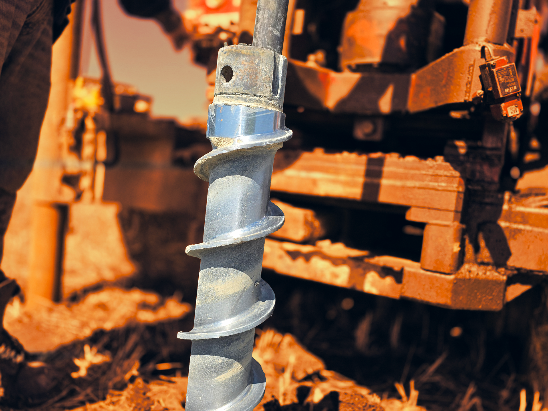 Close-up of a metal auger drill bit with machinery in the background.