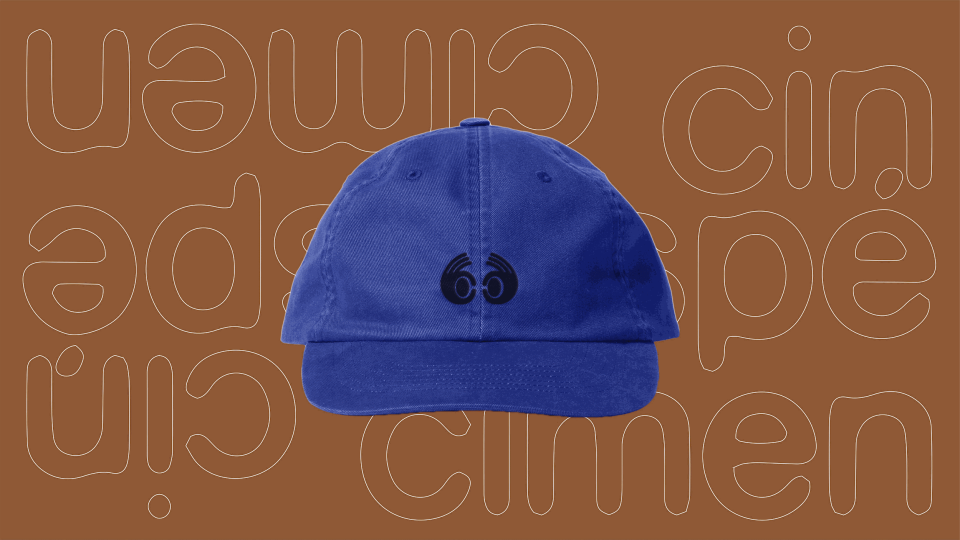 Gorra azul con logo de ojos sonrientes negros, en fondo marrón con borde de líneas blancas formando letras.