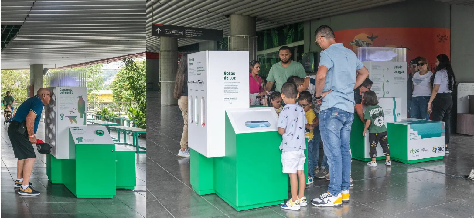 Grupo de personas, adultos y niños, interactuando en exhibiciones educativas sobre gotas de agua y cantores del viento en un espacio público cubierto.
