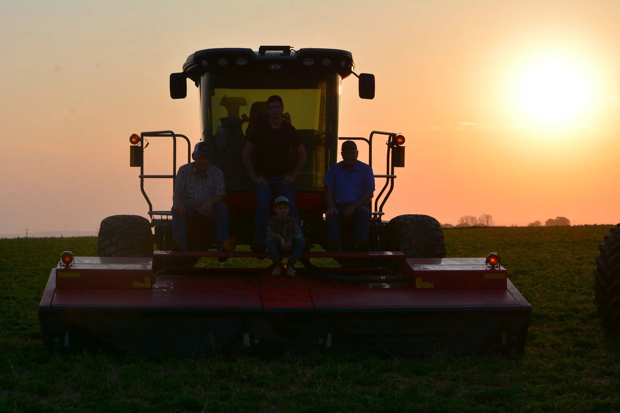 Family posing on a red swather at sunset in a field.