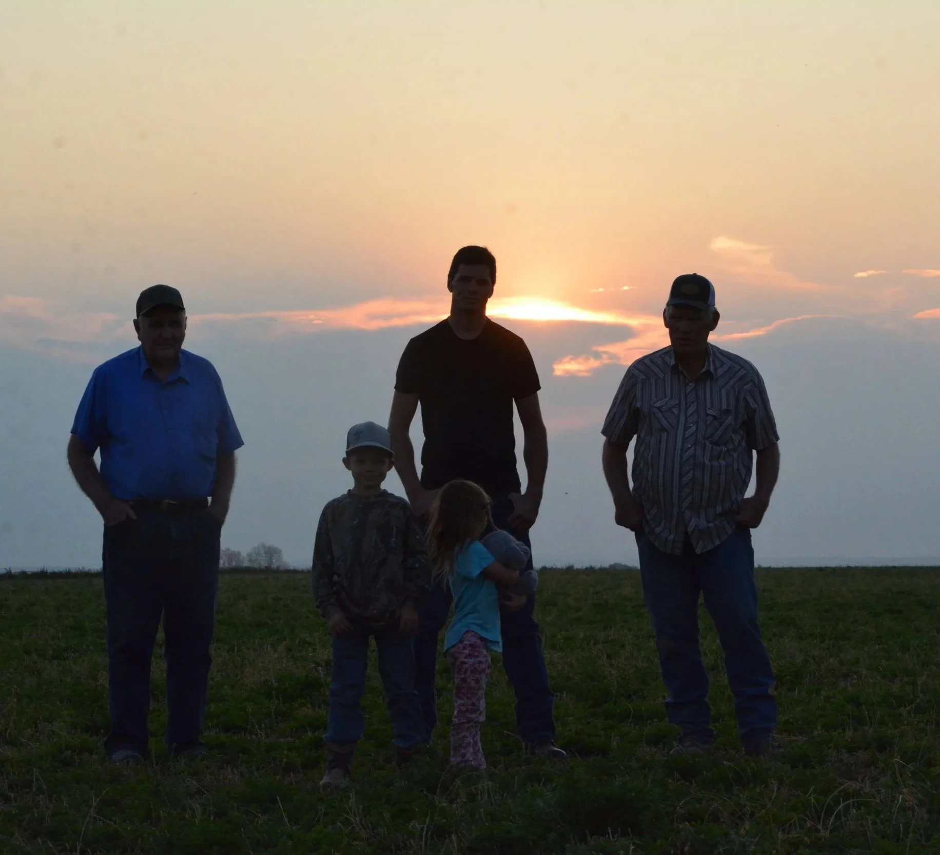 Six people standing outdoors during sunset, including three adults and two children, in a field.