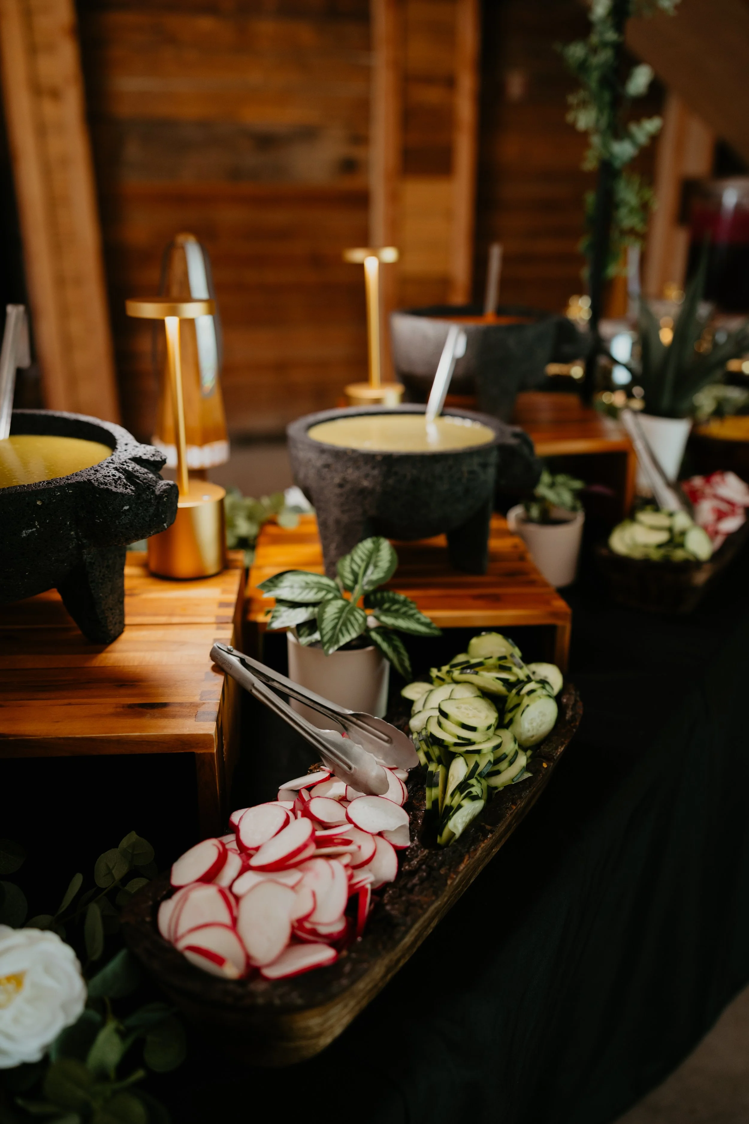 Display of various sliced vegetables including radishes, zucchini, and cucumbers on a wooden tray, with fondue pots in the background.