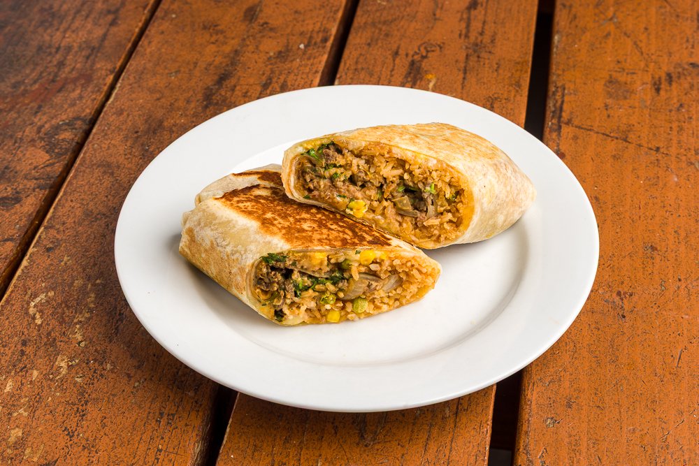 Pierced quesadilla on a white plate with a filling of rice, vegetables, and possibly meat, on a wooden table.