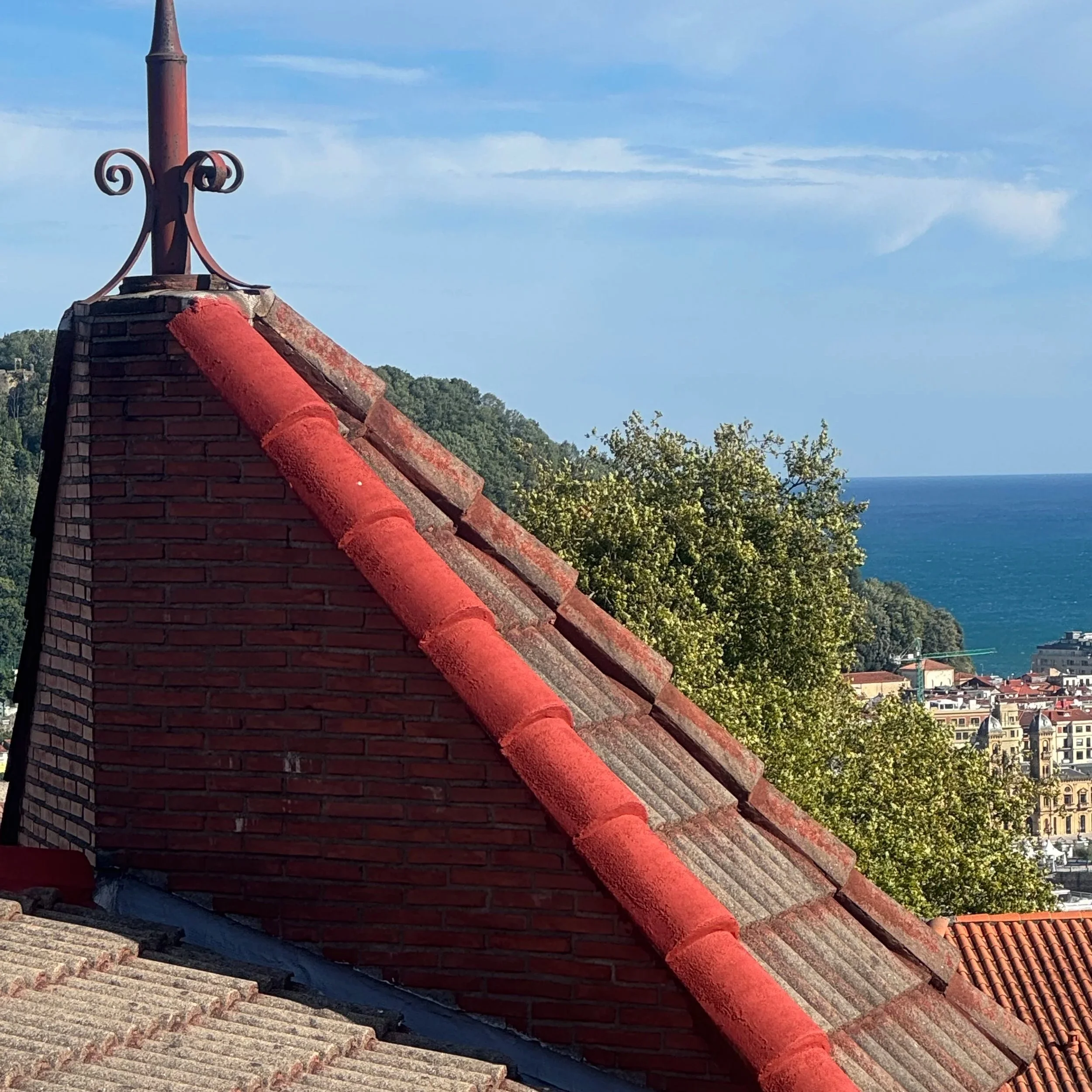 Tejado de tejas rojas con vista del mar y edificios en la ciudad en el fondo, en un día soleado con cielo azul
