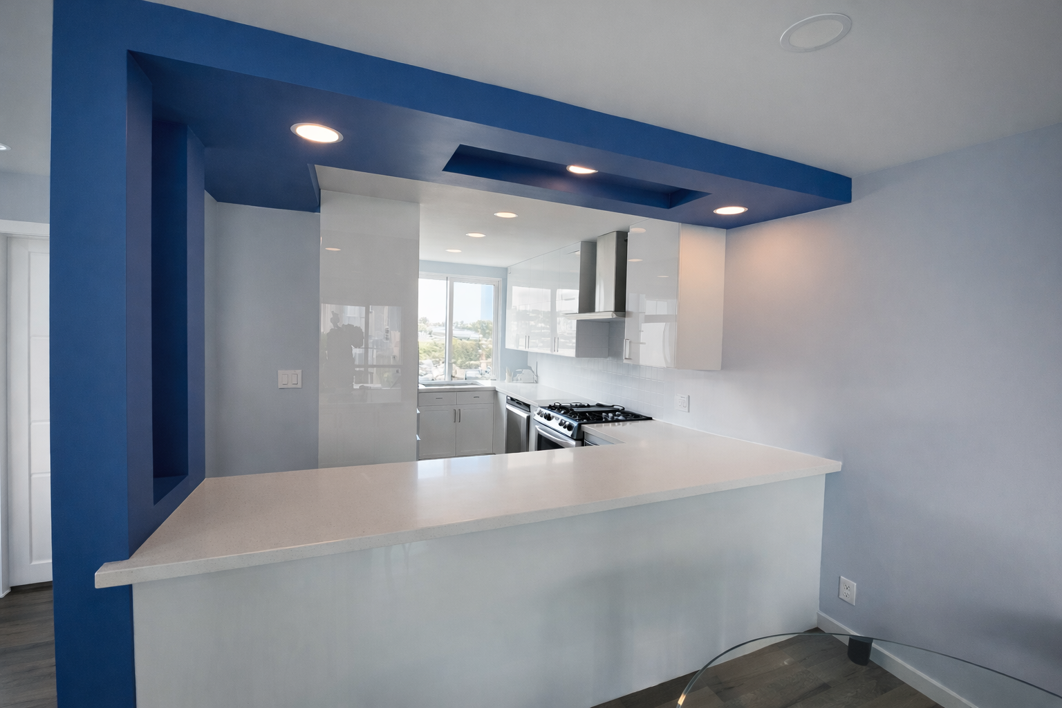 Modern kitchen with white cabinets, stainless steel oven, and a window view, accented by a blue ceiling and wall.