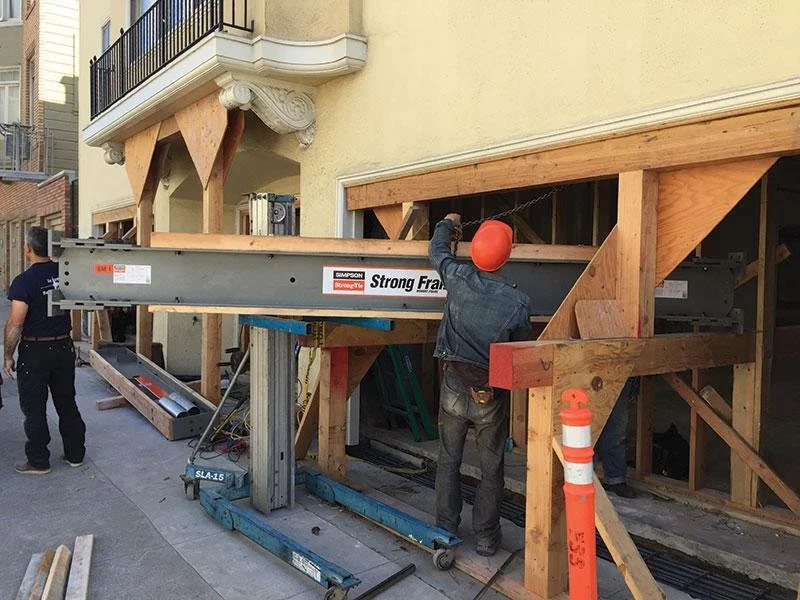 Construction worker in a hard hat working on building a wooden support structure for a building extension.
