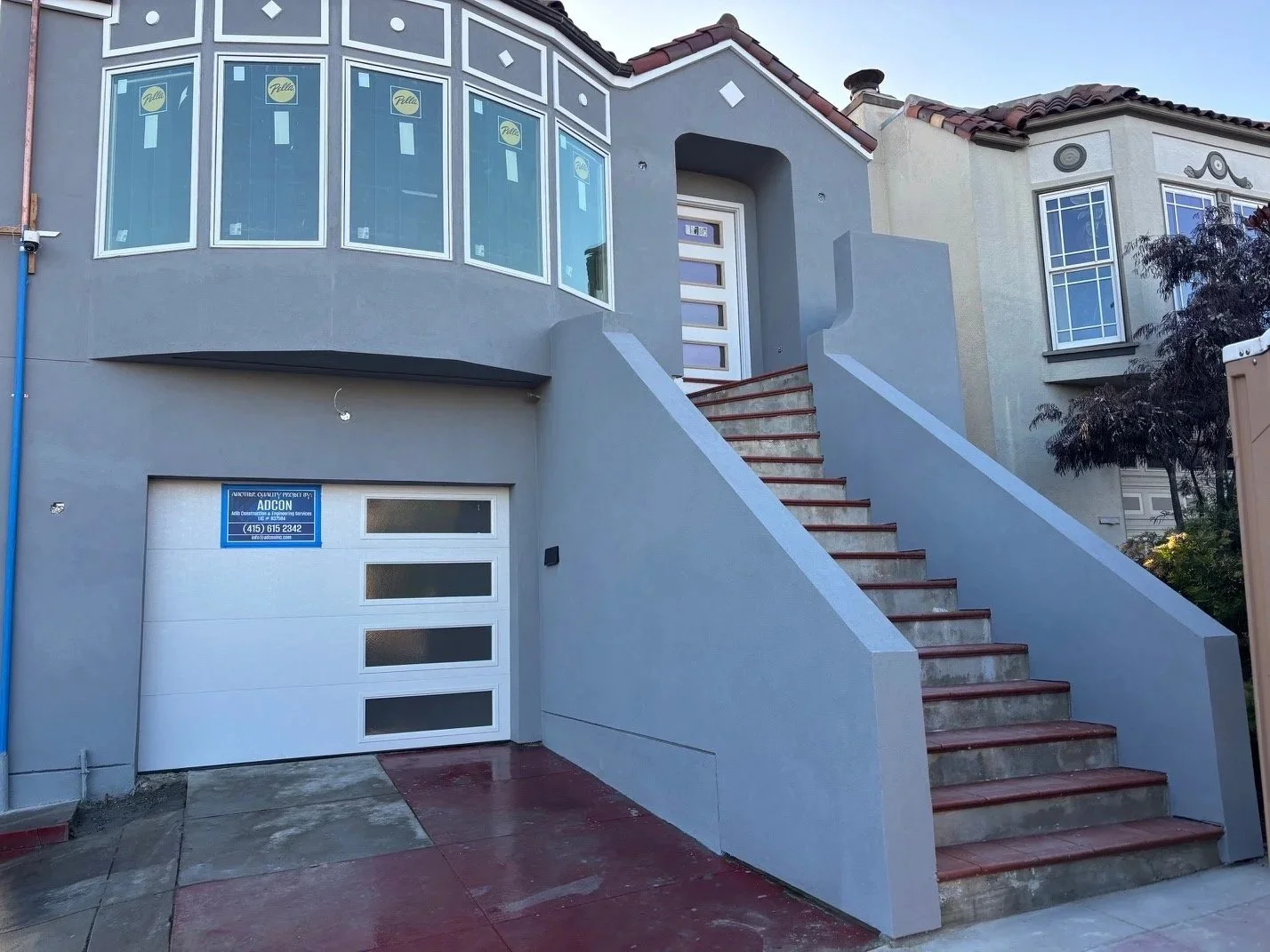 Front view of a modern house with a garage door, stairs leading to the main porch, large windows, and a small tree on the right side.