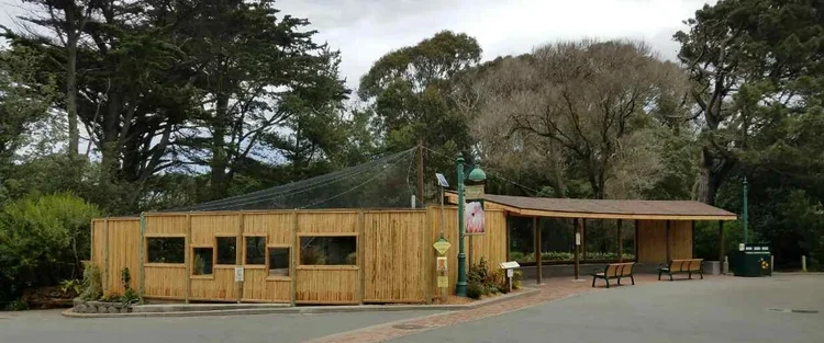 A wooden building with a covered patio and benches in a park setting, surrounded by trees.