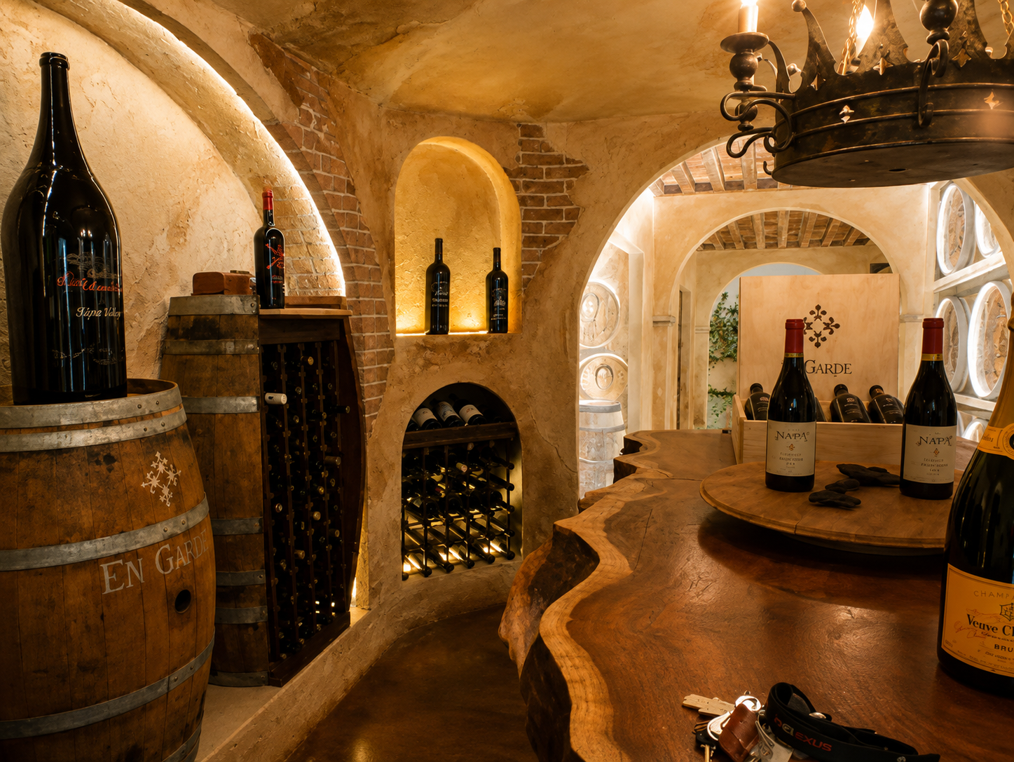 Wine bottles on barrels and shelving in a rustic wine cellar with arched brick walls and a chandelier.