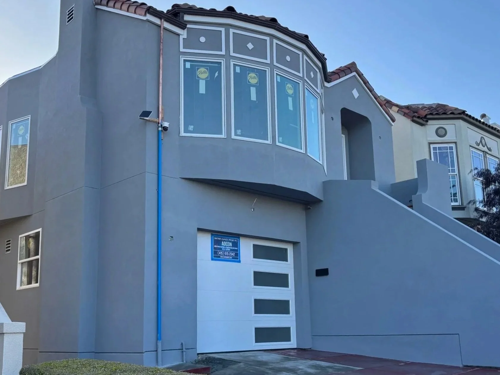 White modern two-story house with black door, glass garage door, staircase on right side, and small landscaped yard with rocks.