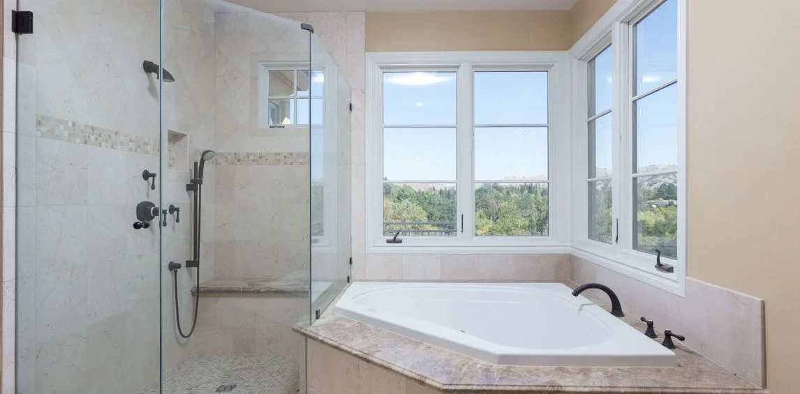 Bathroom with a glass-enclosed shower and a large bathtub next to windows with a scenic view.