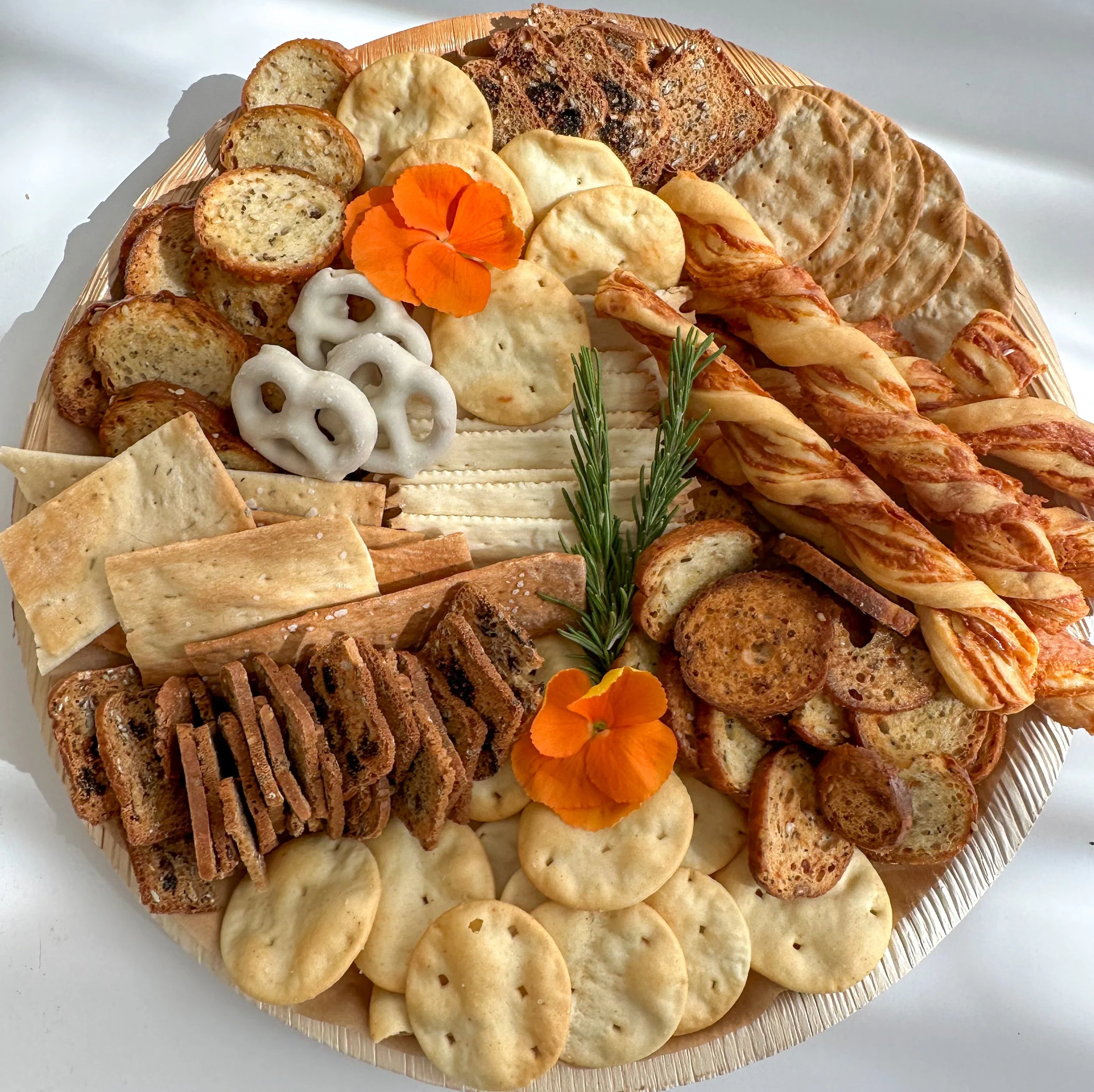 Holiday cheese and snack platter with crackers, dried fruit, nuts, gingerbread cookies, candy canes, white chocolate, and rosemary sprigs on a round wooden tray.