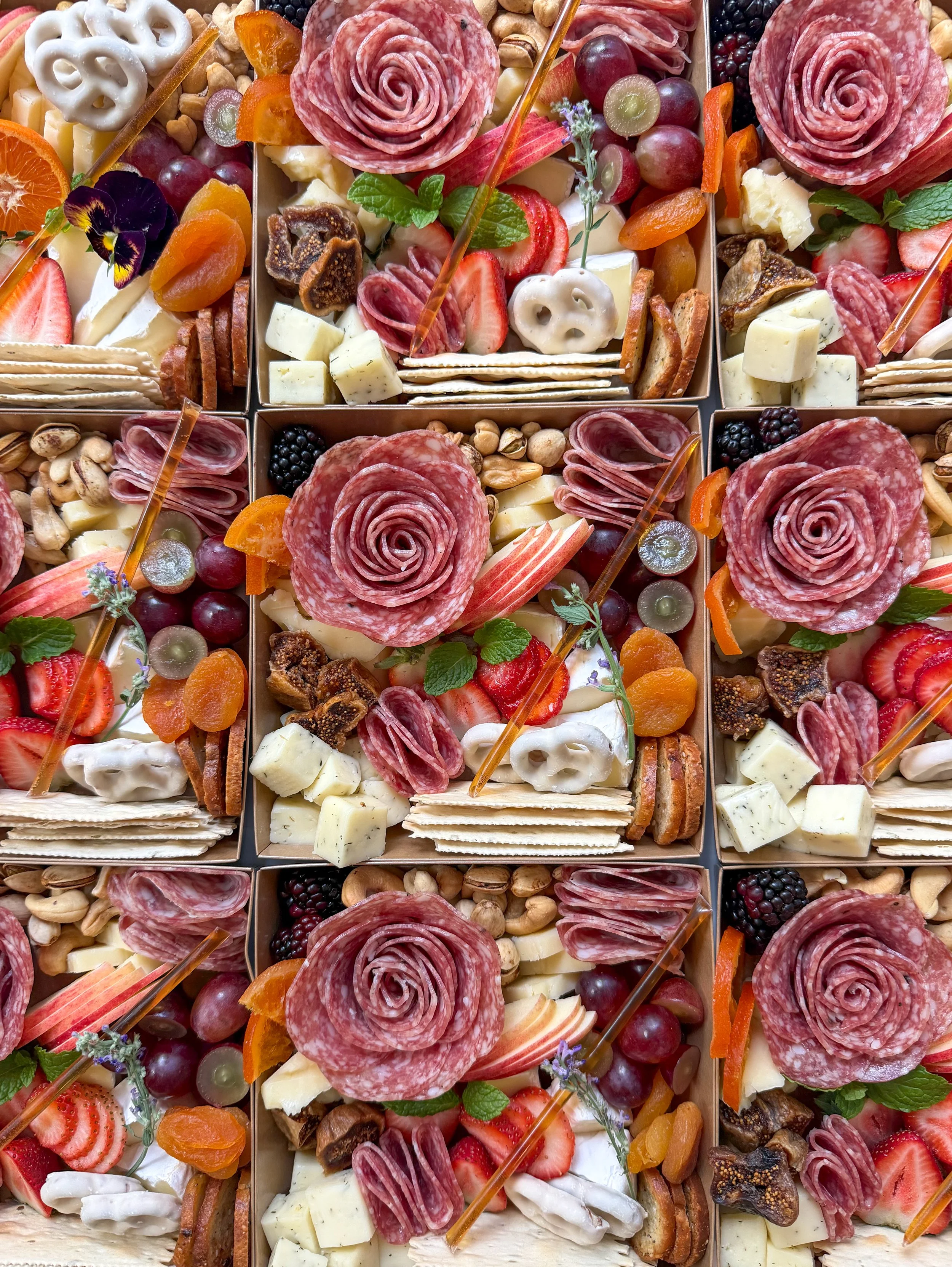 A charcuterie board with various cheeses, sliced meats, fresh strawberries, blackberries, green grapes, figs, figs, and slices of cucumber and honey. There is also a honey dipper, herbs, and a small jar labeled 'Kraze Board' in the center.