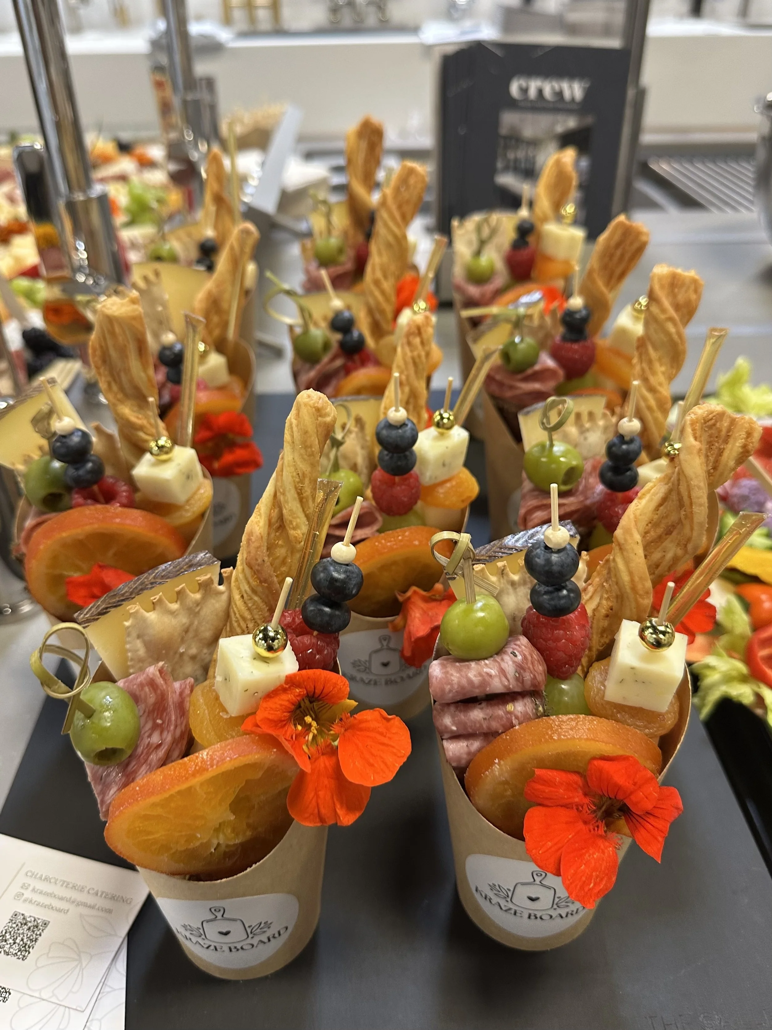 A platter of colorful fruit and meat appetizers garnished with edible flowers, cheese, and crackers, topped with skewers of grapes and berries.