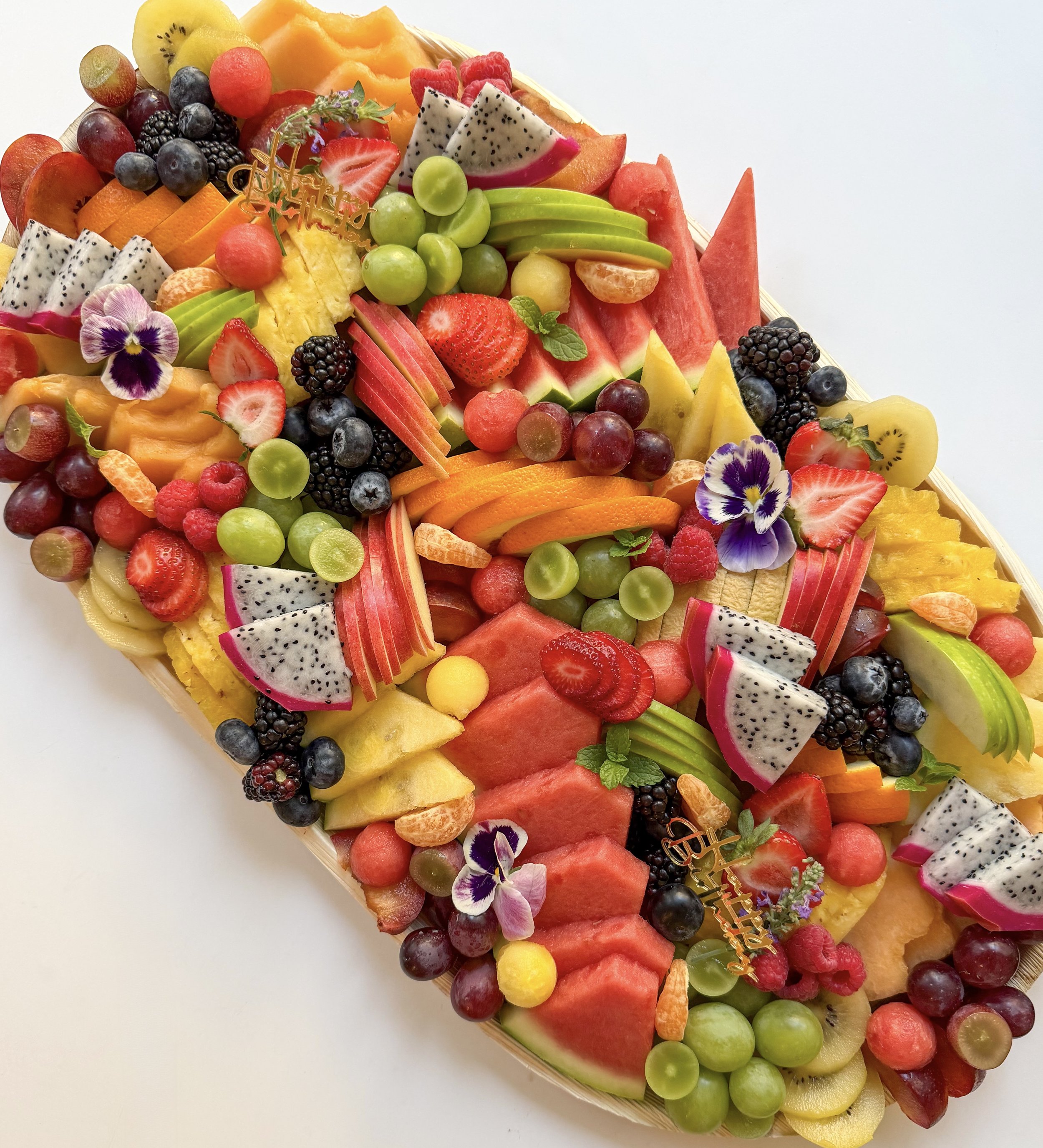 A colorful fruit platter featuring strawberries, blackberries, blueberries, watermelon, cantaloupe, honeydew, orange slices, pomegranate seeds, kiwi slices, and garnished with mint leaves.