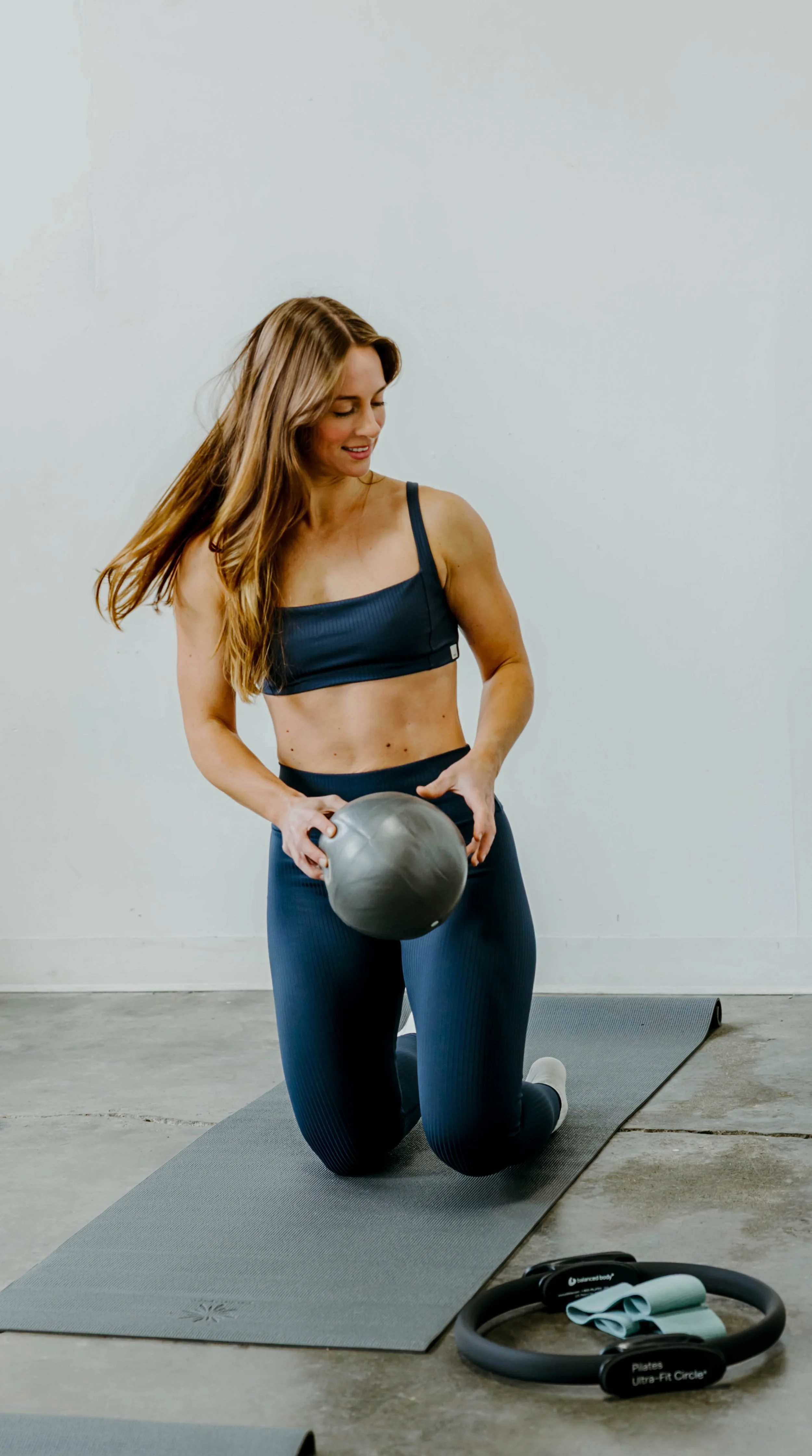 Woman in blue workout set on her knees with Pilates props.