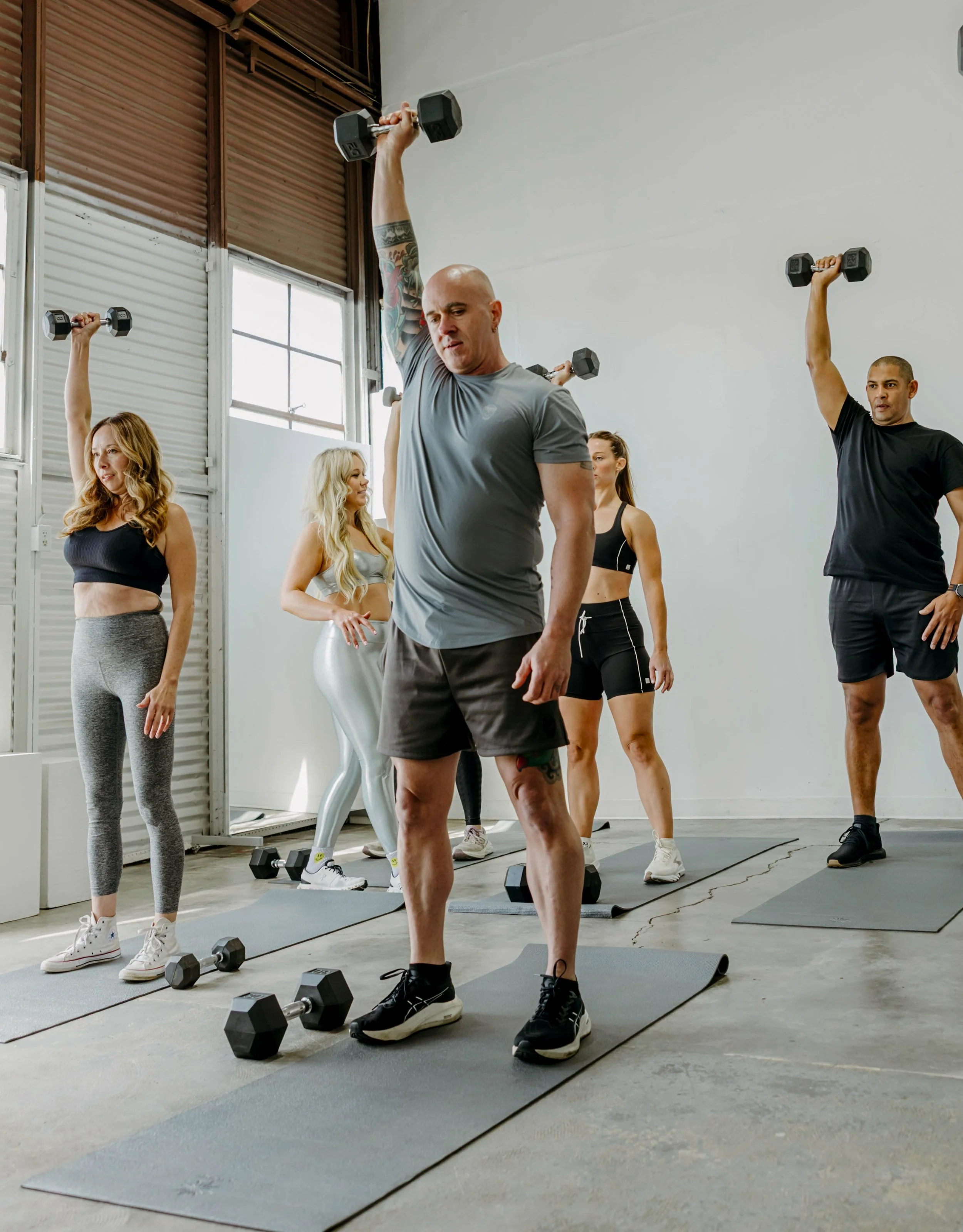 Group of people pushing weights overhead standing on yoga mats.
