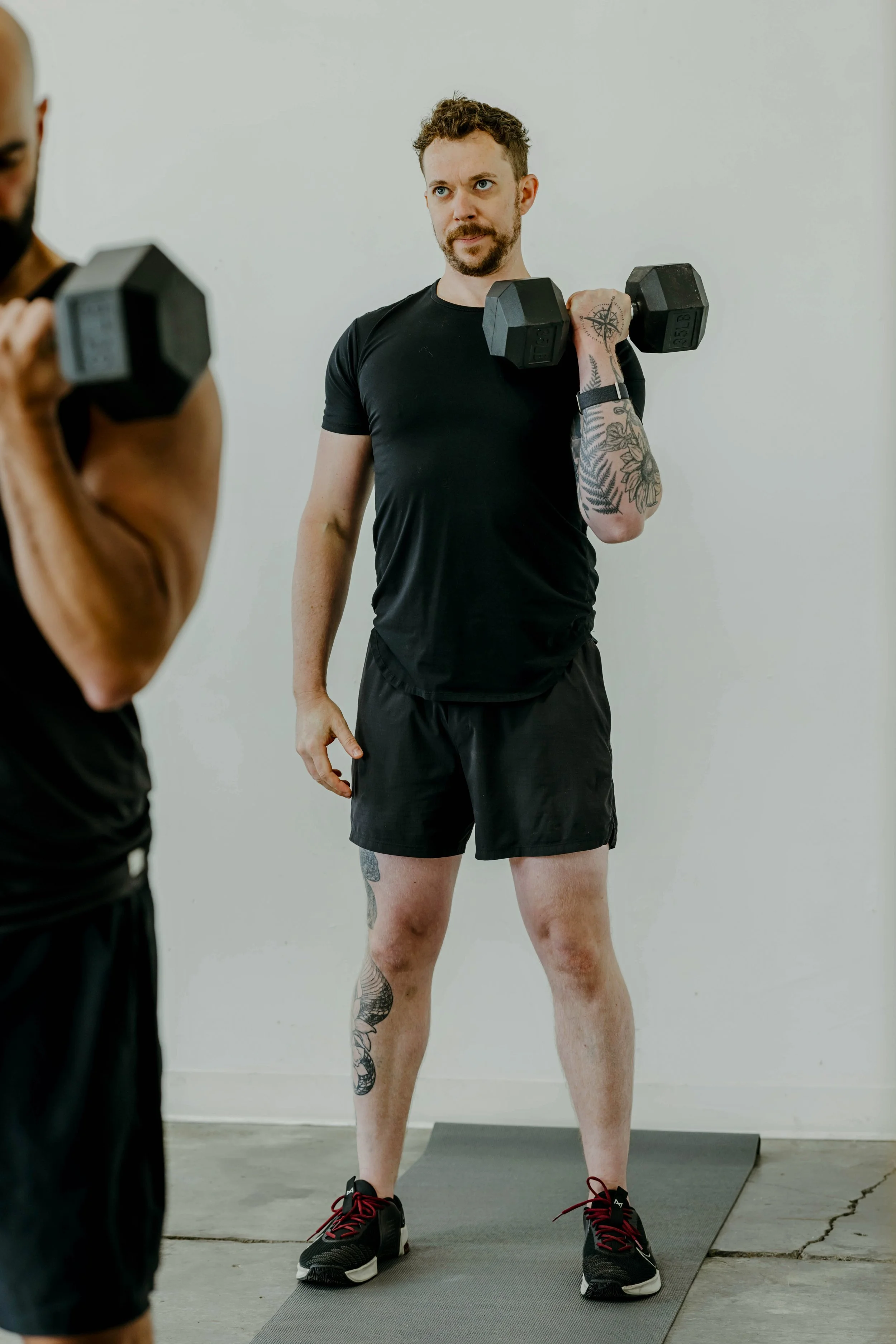 Man in black shorts and T-shirt with tattoos lifting weight