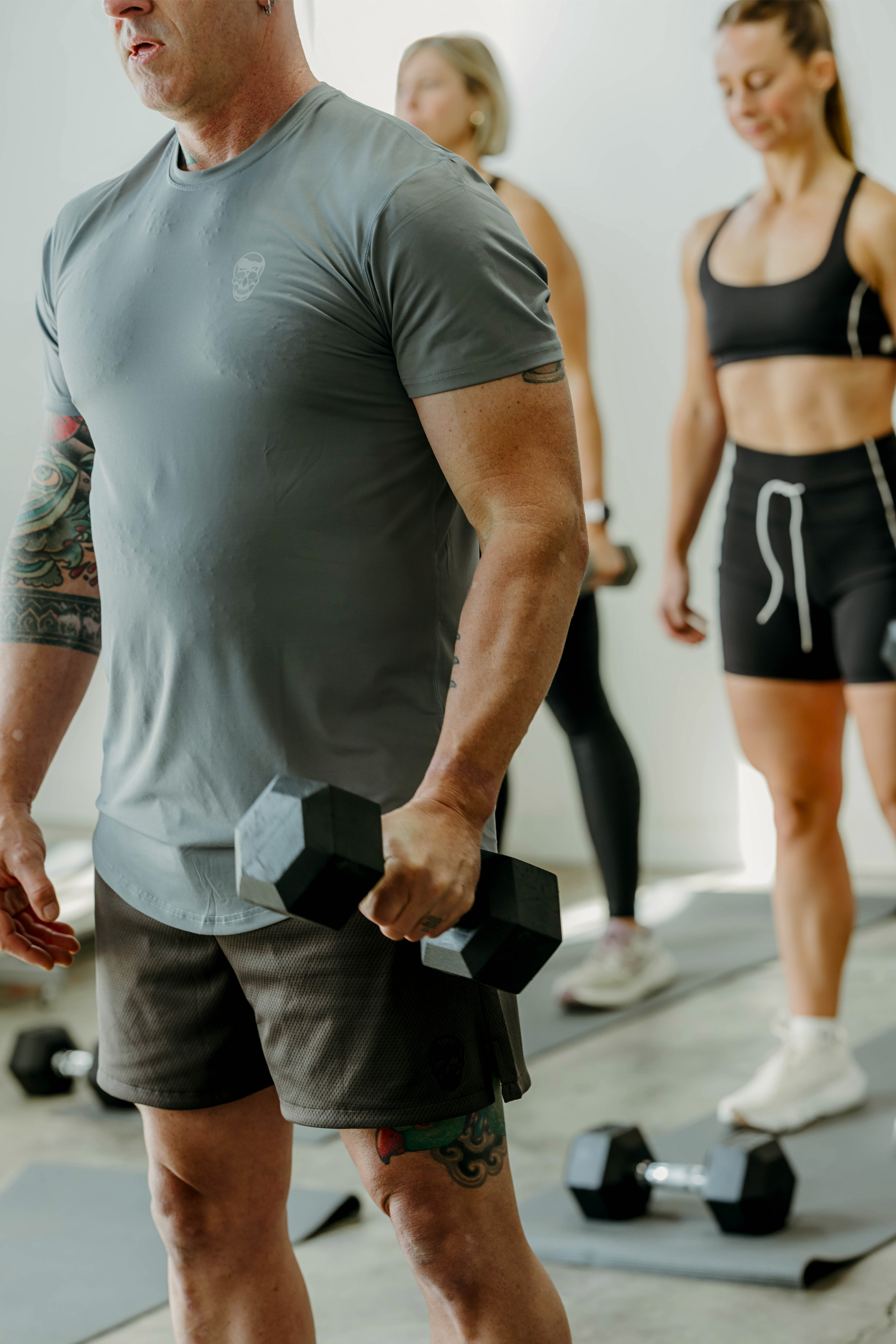 Man in foreground holding weight, women in background holding weights