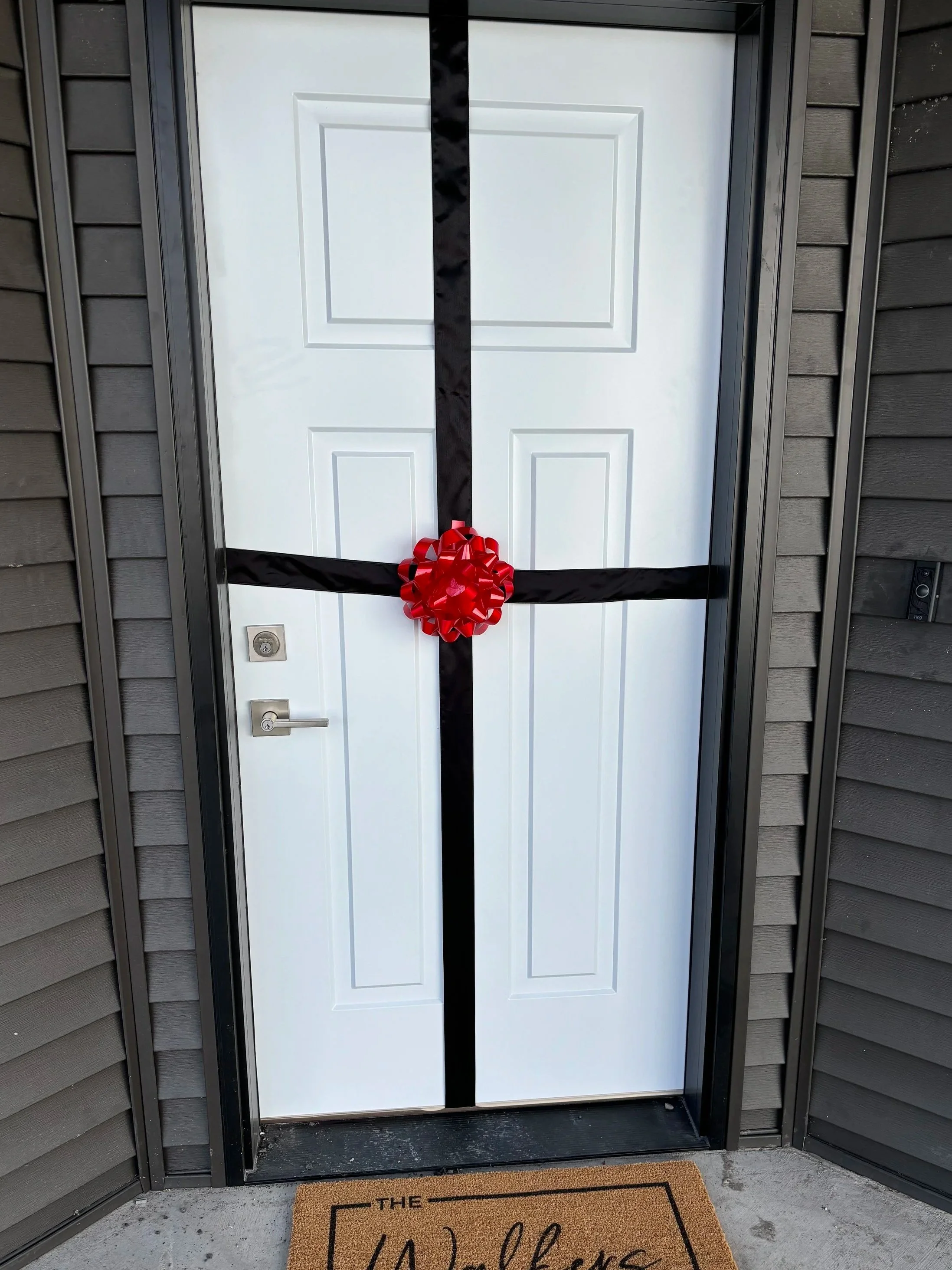 Front door decorated with a black ribbon and red bow, with a doormat that reads "The Walkers." real estate closing gift