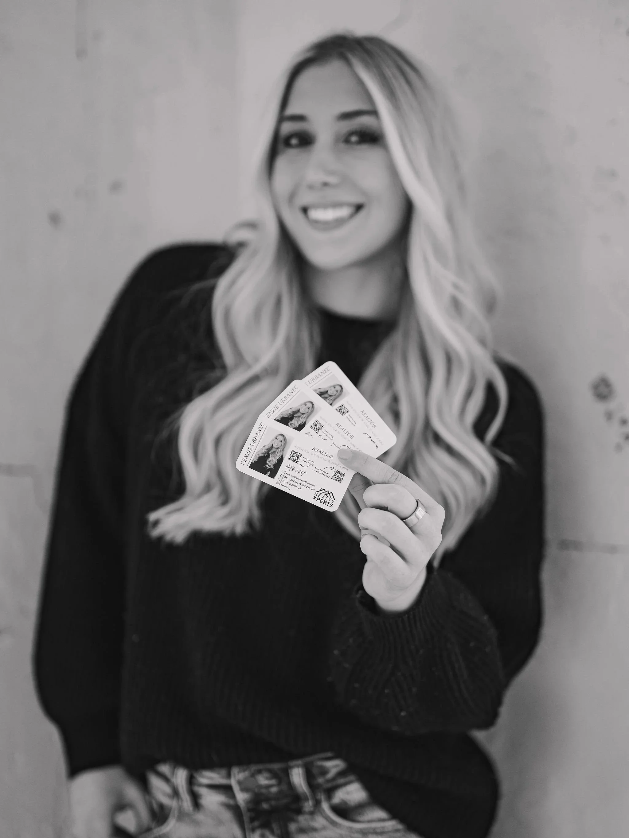 A realtor with long wavy blonde hair holding two ID cards and smiling.
