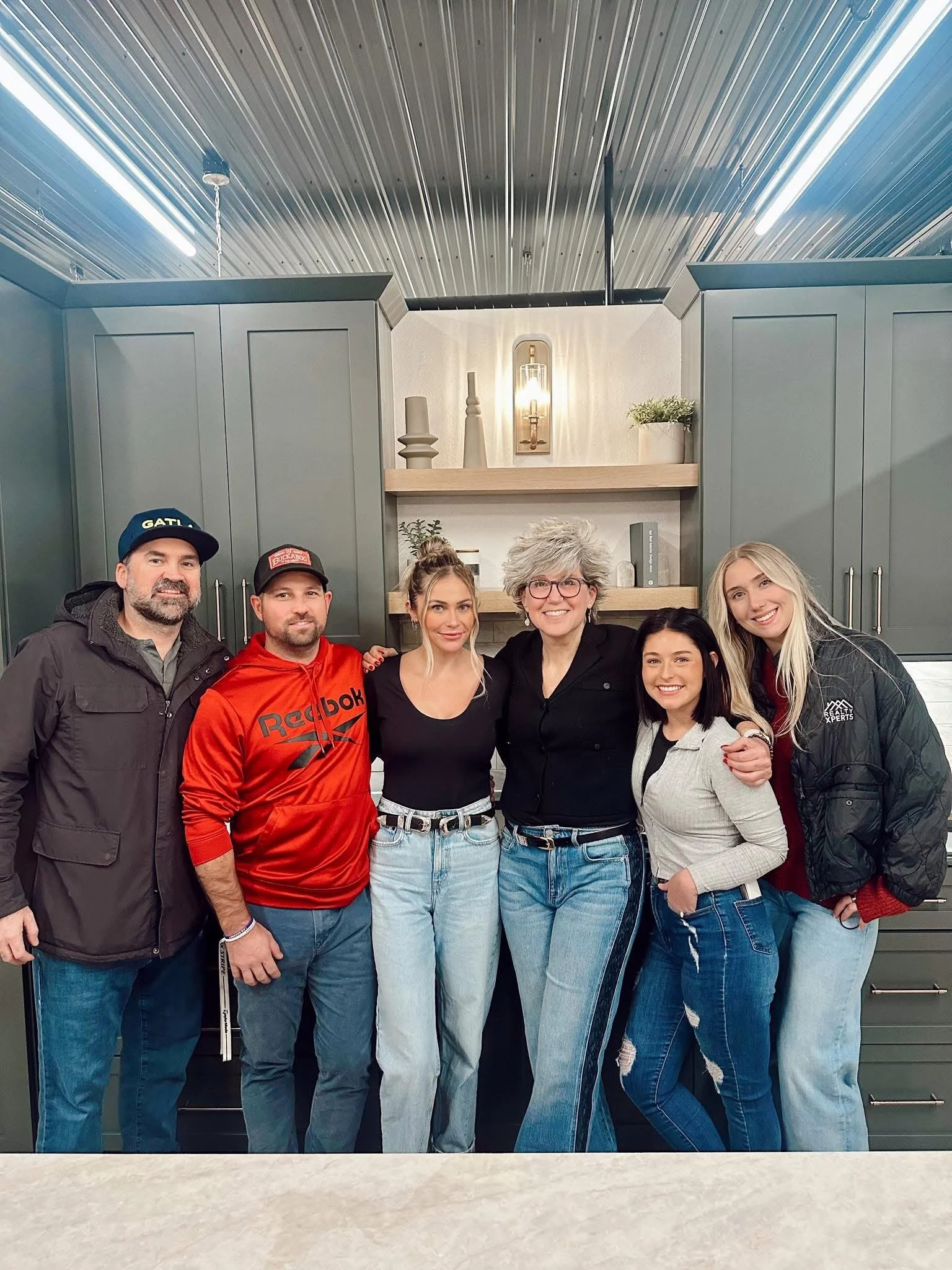 Realty Xperts partners/realtors at Jordahl Custom Homes christmas party. Group of six people standing together in a kitchen, smiling for the camera.
