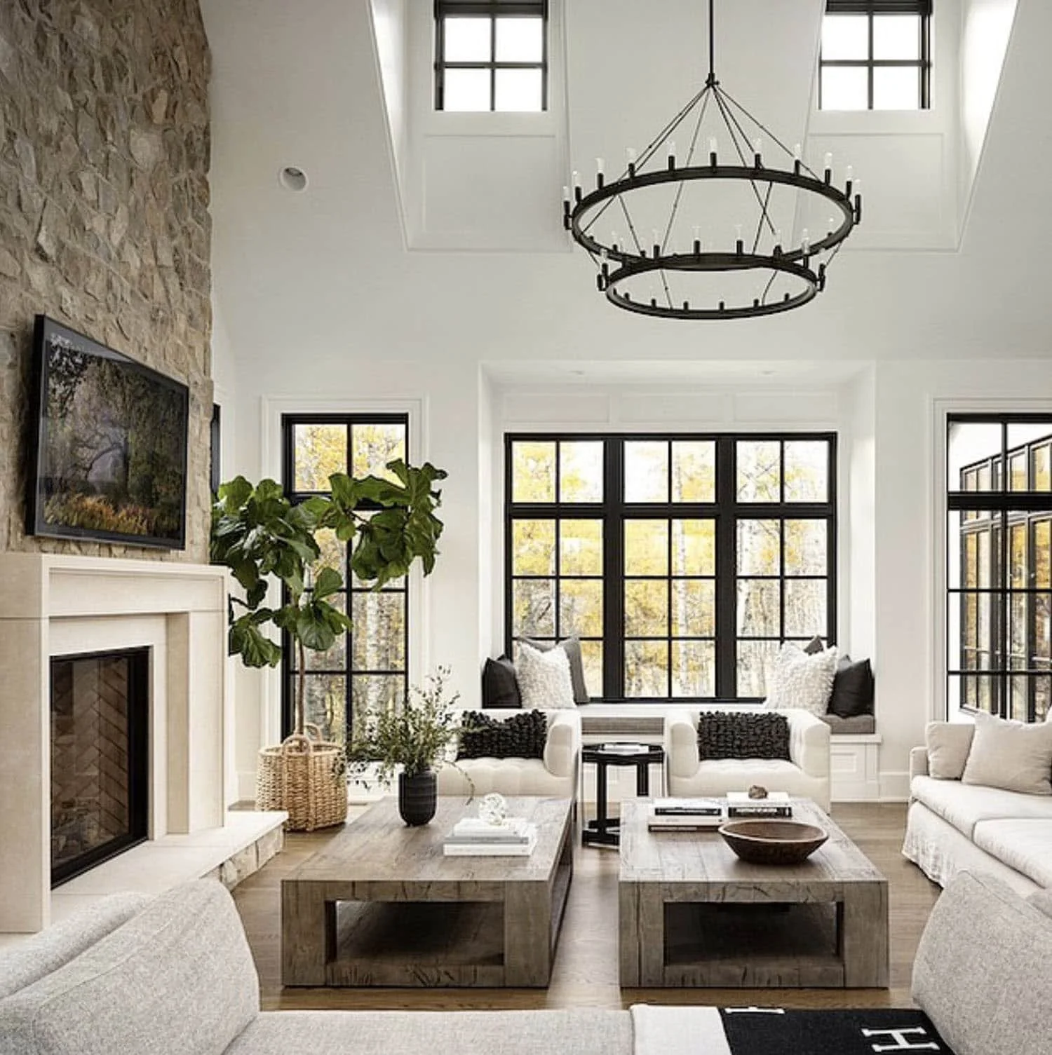 Bright and airy living room with large black-framed windows, white sofas, a stone fireplace, and a black circular chandelier hanging from the ceiling