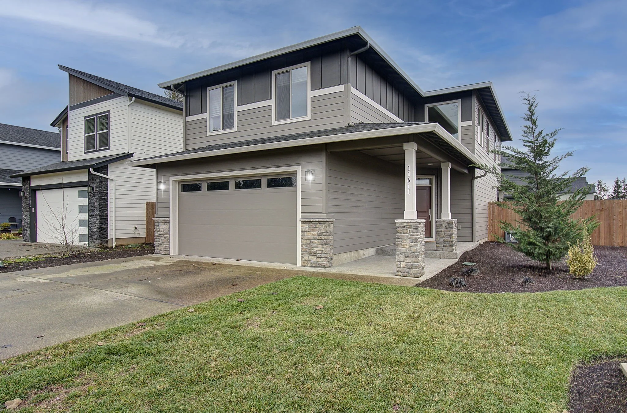 Modern two-story home with gray siding, stone accents, covered porch, two-car garage, and landscaped yard in a newer Southwest Washington neighborhood.