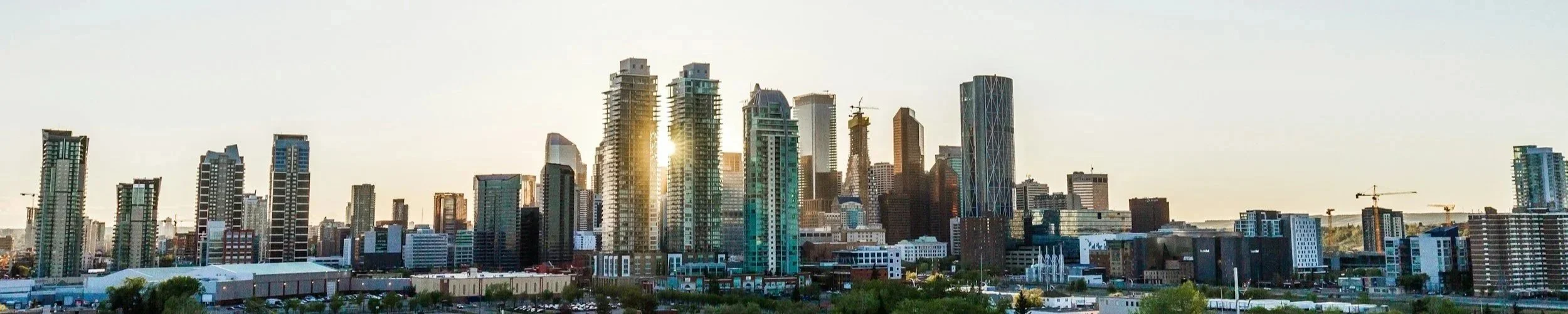 Sunset view of Edmonton city skyline with tall skyscrapers, some under construction, and a few cranes in the background.