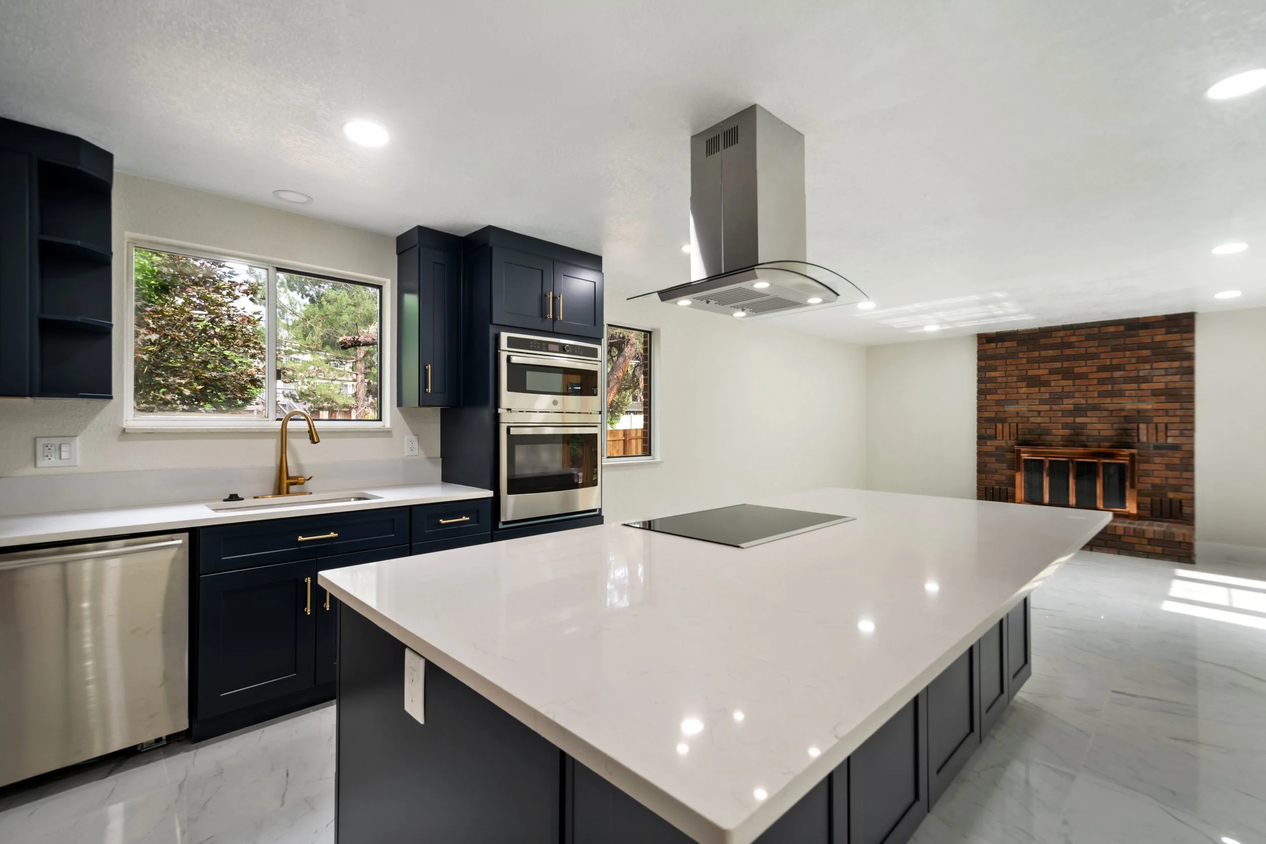 Modern kitchen with navy cabinets, white countertops, stainless steel appliances, and a brick fireplace in the living area.