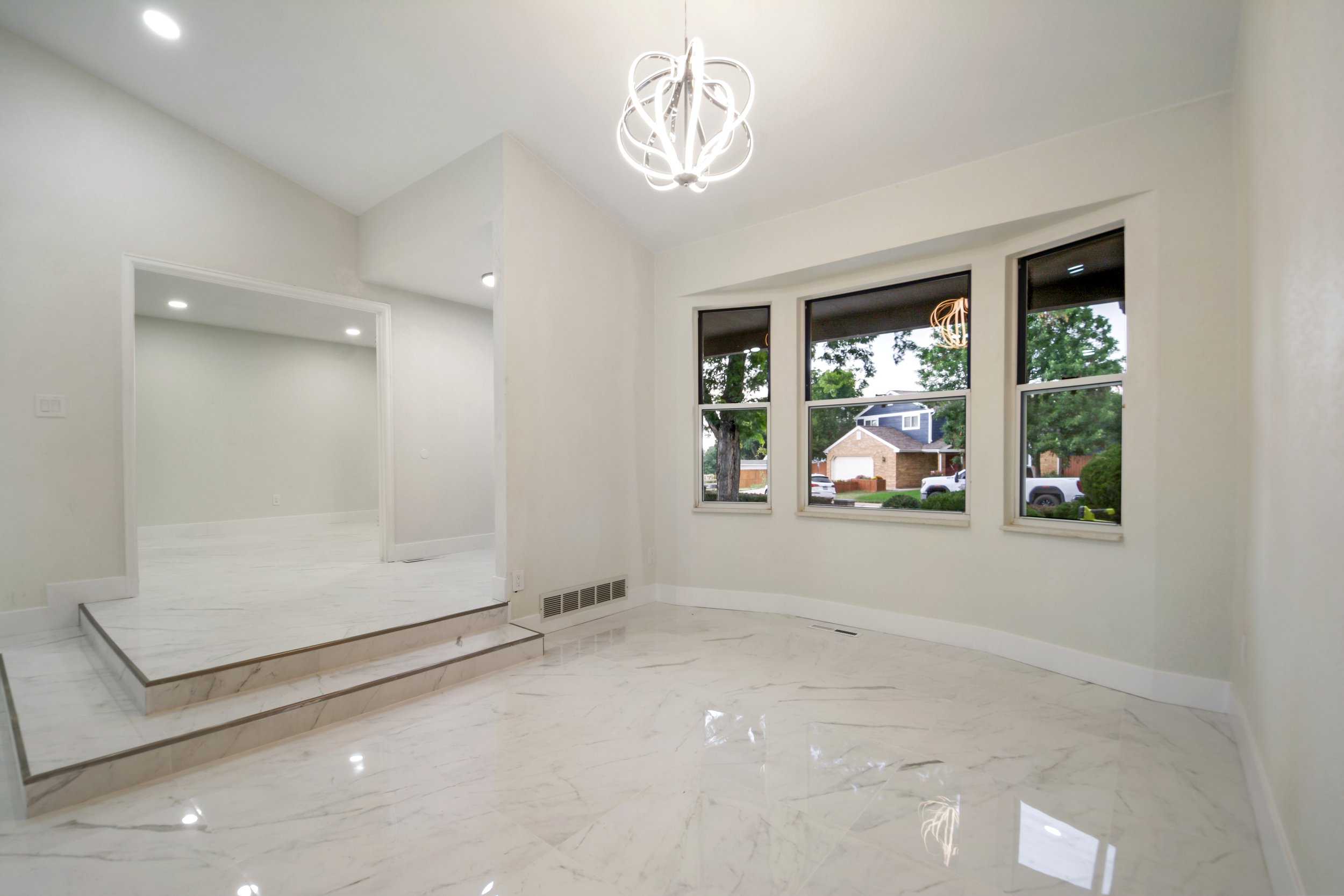 Empty room with white marble floors, white walls, large window, and modern chandelier lighting