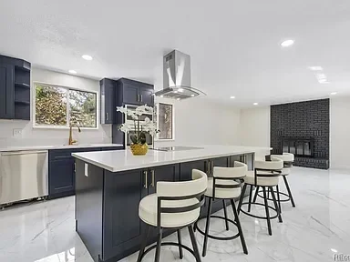 Modern kitchen with navy blue cabinets, white countertops, a central island with four white bar stools, and a large window with a view of trees.