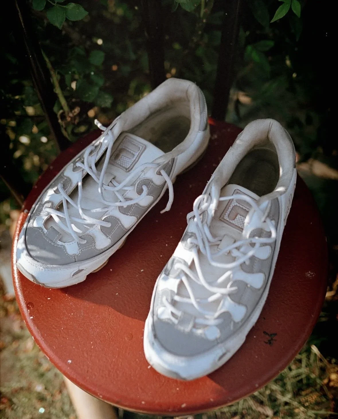 White and gray sneakers placed on a red round surface outdoors.