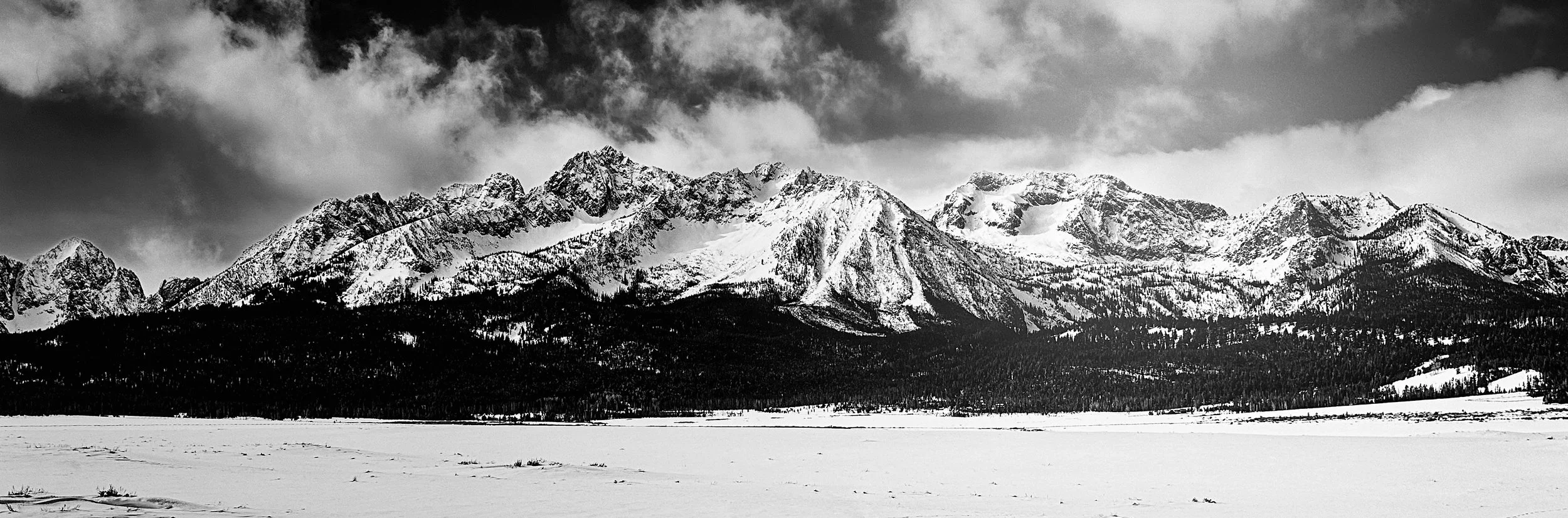 David Nehmer — "Sawtooth Silence," Sawtooth Range, 20"x60" ($600 value)
Shot at zero degrees after snowshoeing in to get the angle, this black-and-white panorama catches the Sawtooths mid-storm, snow still moving across the peaks. Photography runs th