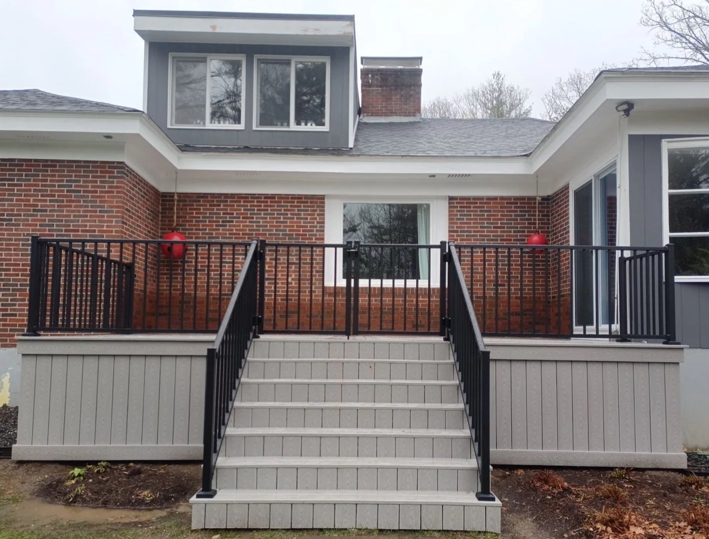 Backyard patio with stairs, black railing, brick house wall, window, sliding door, and two red lanterns