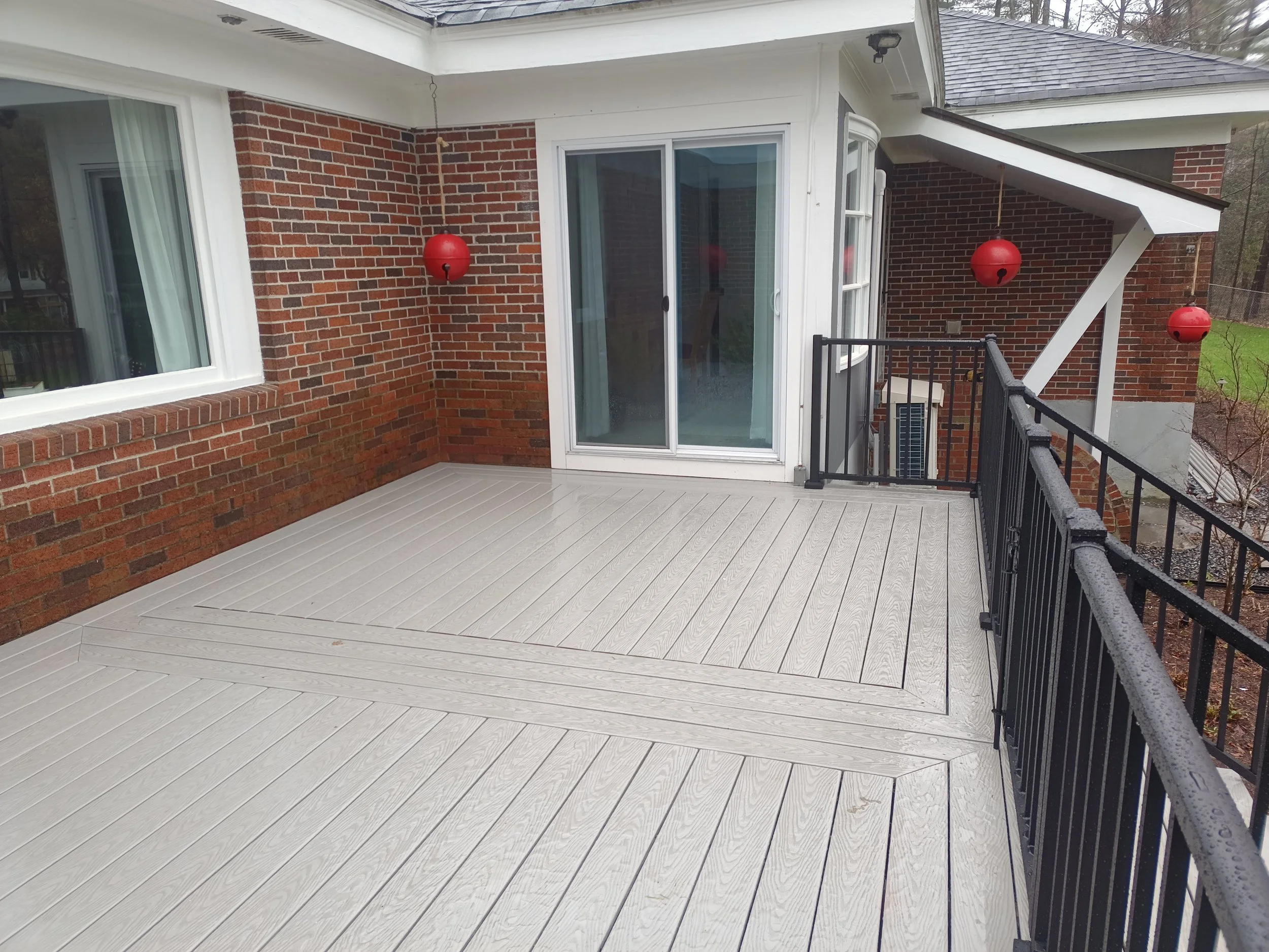 Empty balcony with white wooden flooring, brick walls, black metal railing, and three hanging red lanterns