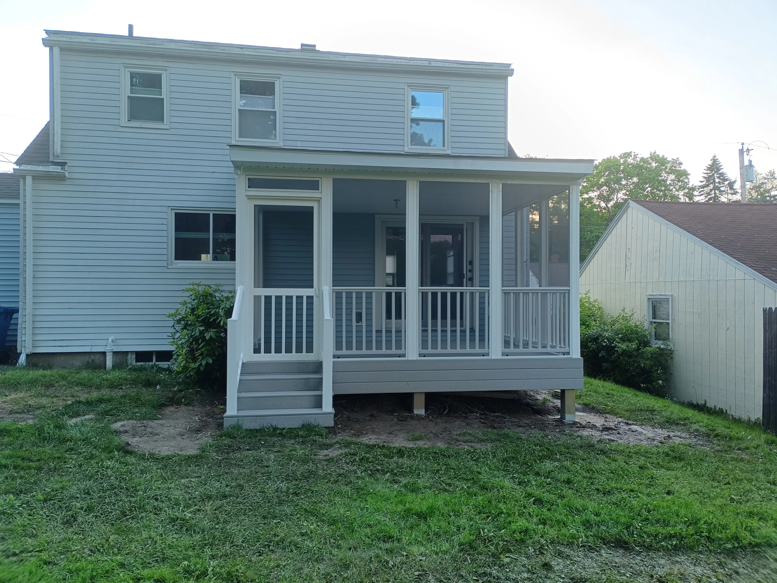 A two-story house with a screened porch in the backyard, with a small set of steps leading up to it, and some greenery around it.