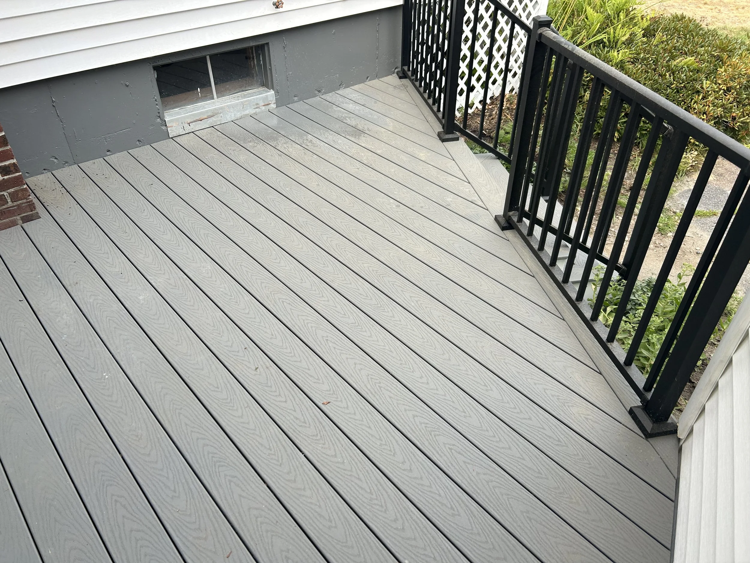 Gray composite deck with black railing and white lattice privacy screen in residential backyard.