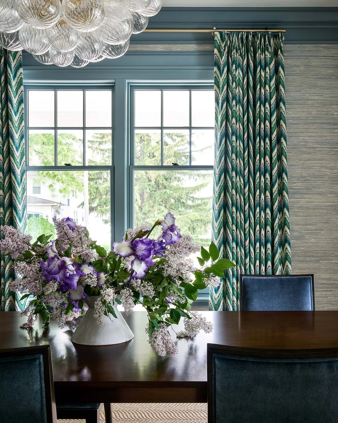 Dining room with blue paneled walls, statement glass chandelier, and floral centerpiece in Kenilworth residence.