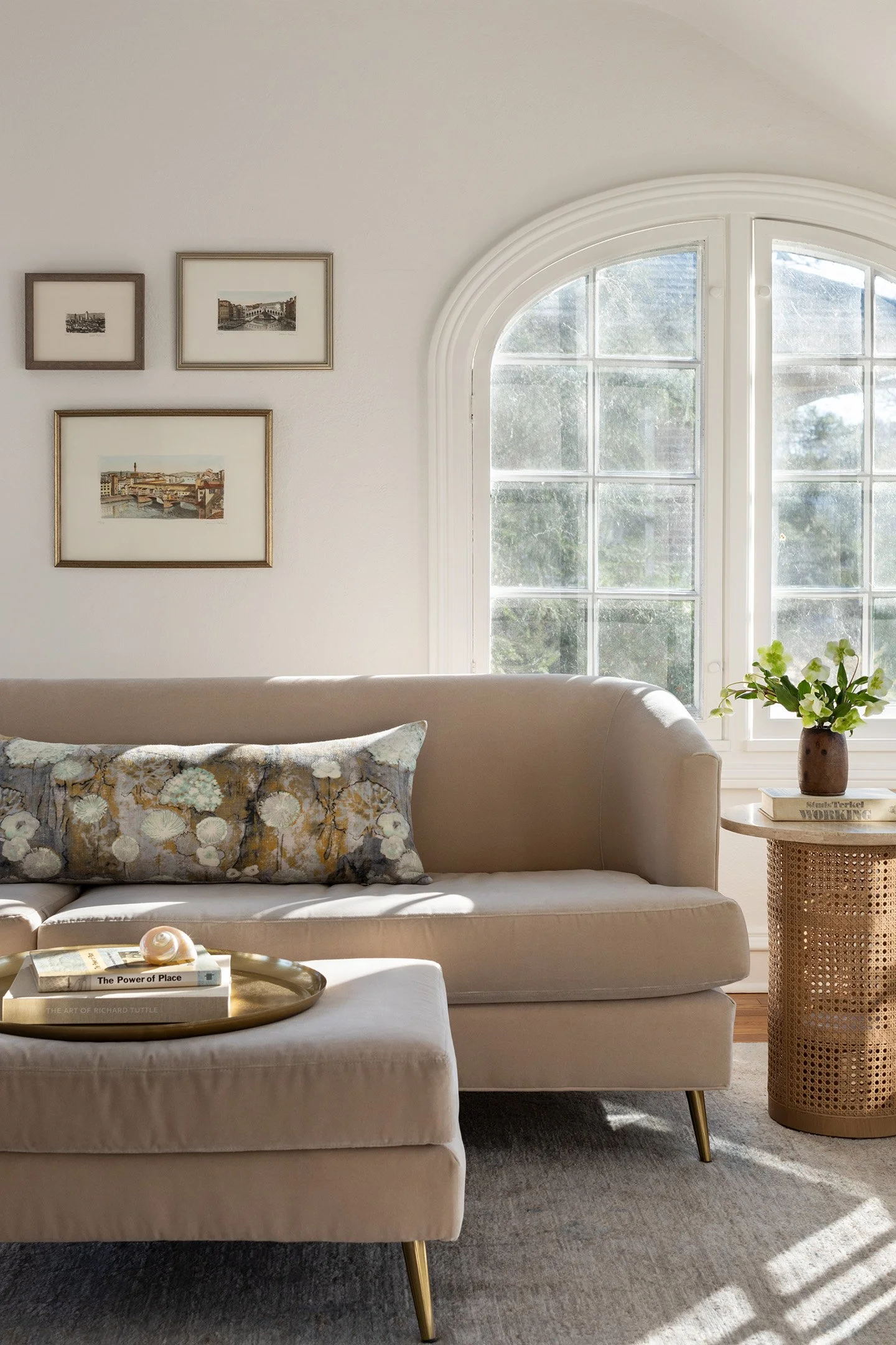 Living room with arched window, neutral sofa, brass tray ottoman, and woven side table.