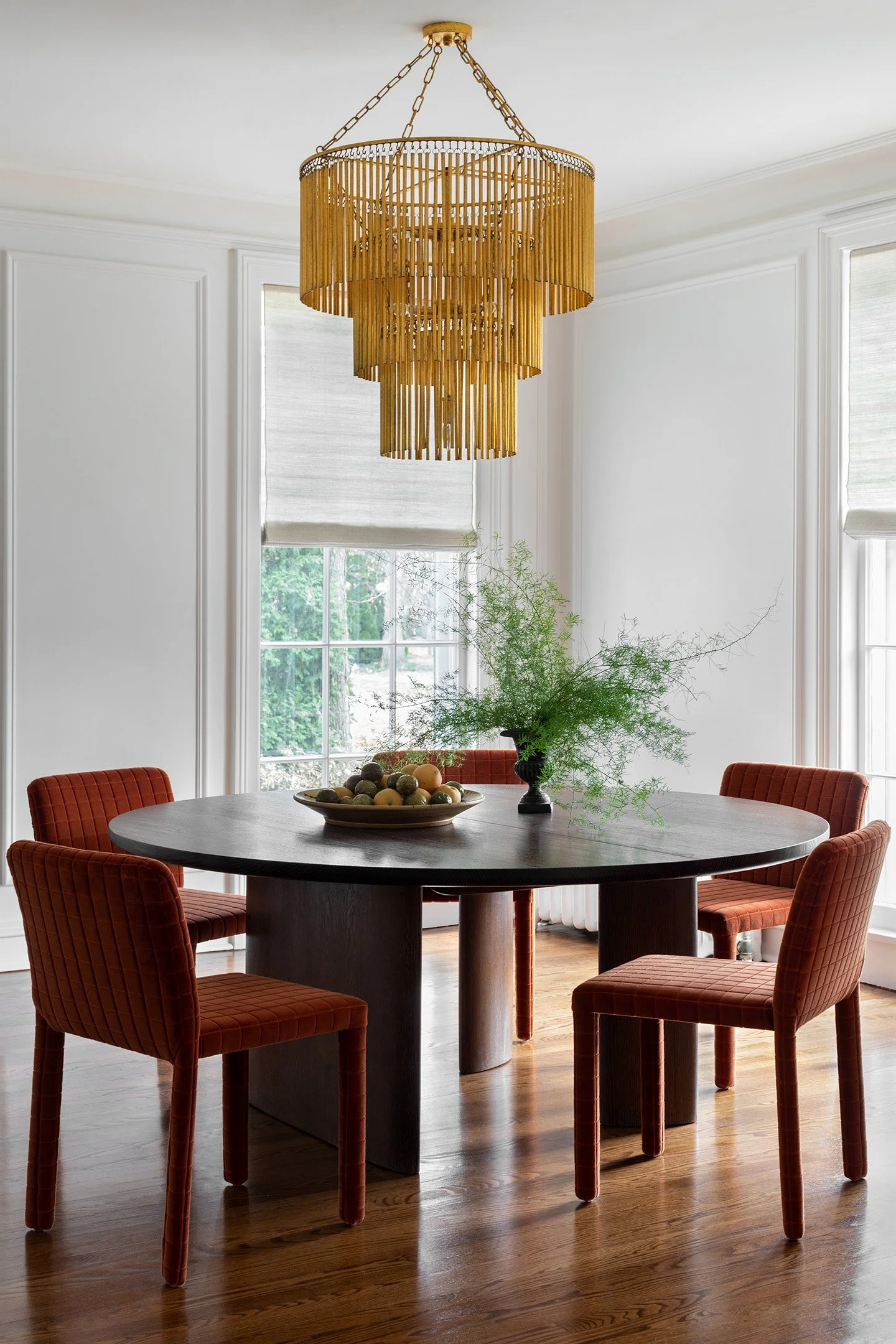 Dining room with round wood table, rust upholstered chairs, and tiered brass chandelier.