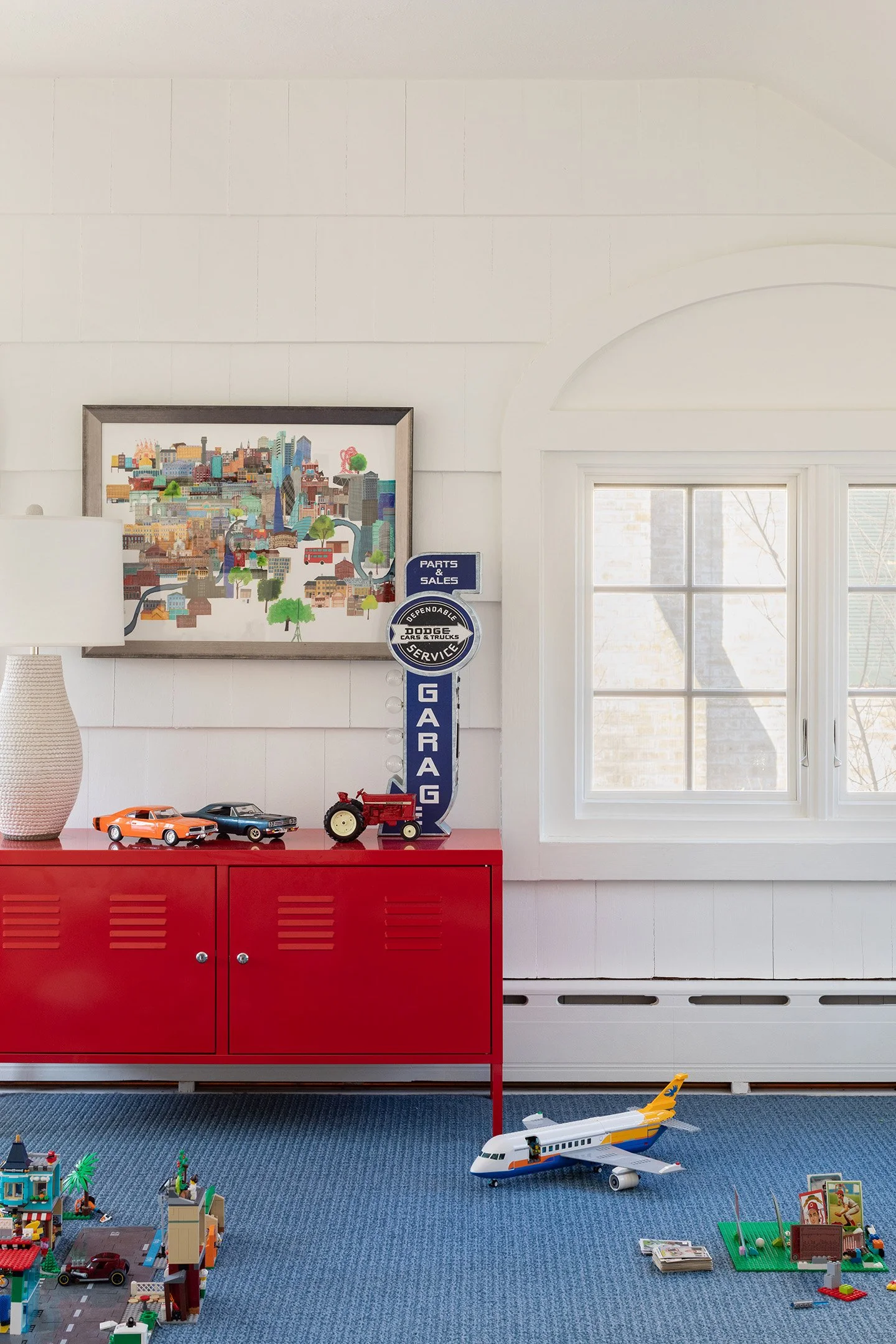Kids playroom with red storage cabinet, vintage garage sign, toy cars, and blue carpet flooring.